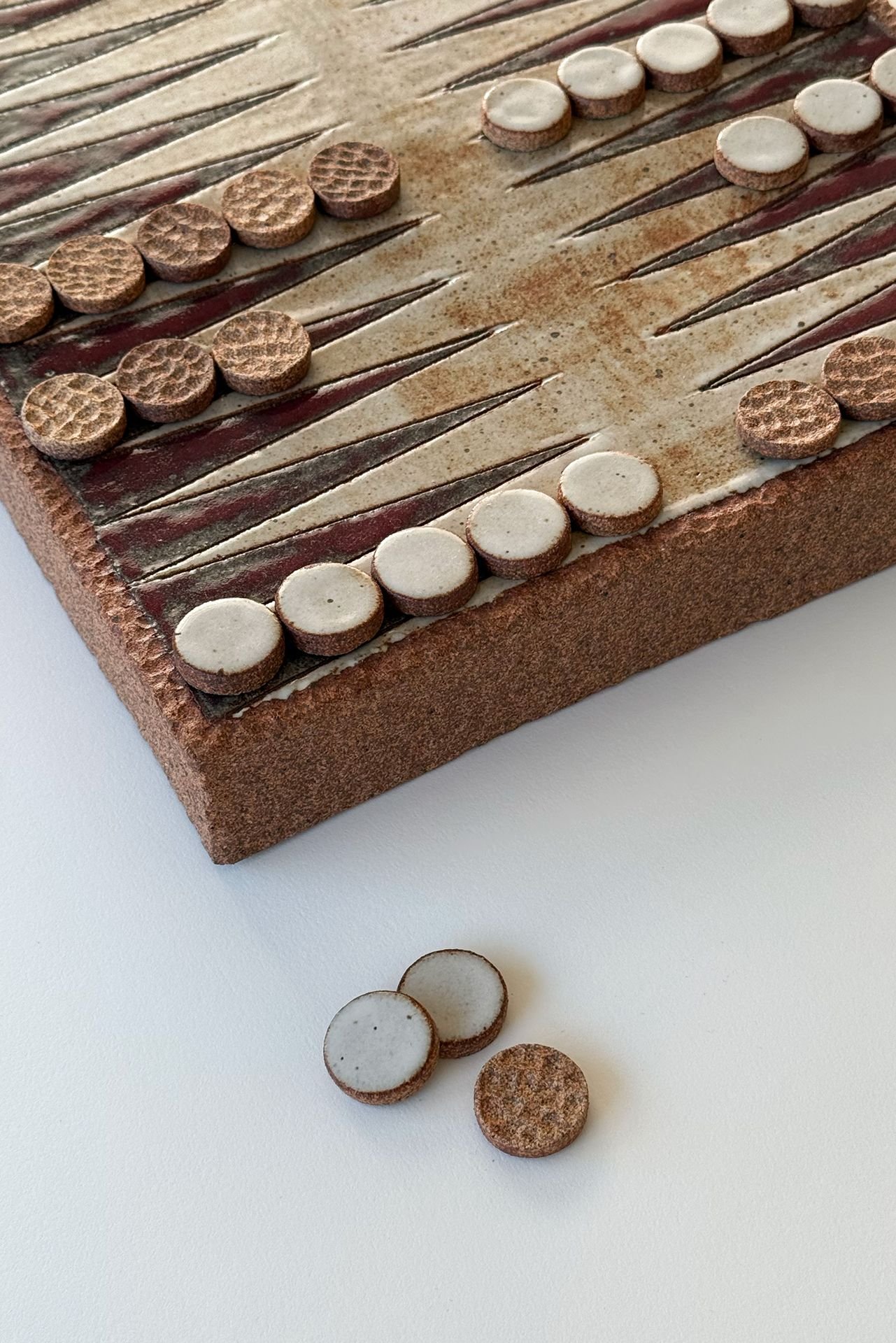 Close-up of a vintage backgammon game board with checkers placed on it, some scattered on a white surface outside the board.
