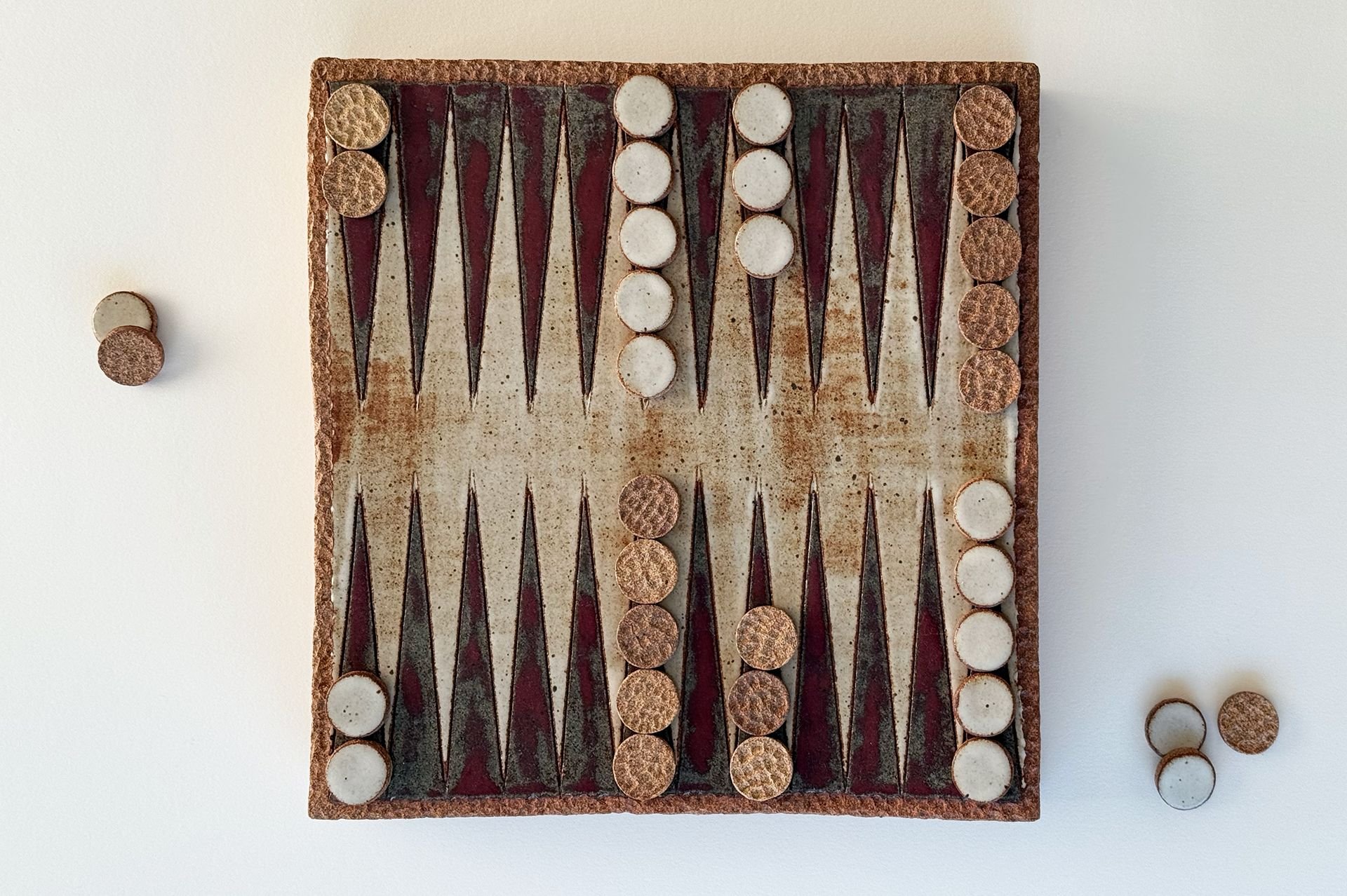 A vintage backgammon board with round checkers on a white surface, some checkers are on the board, others are off to the side.