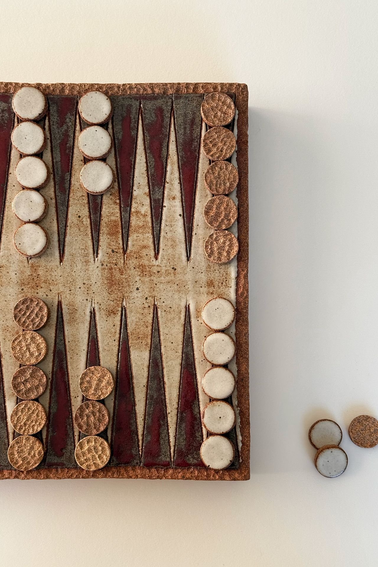 Close-up of a vintage backgammon game with round checkers and pointed pieces on a board next to a white wall.