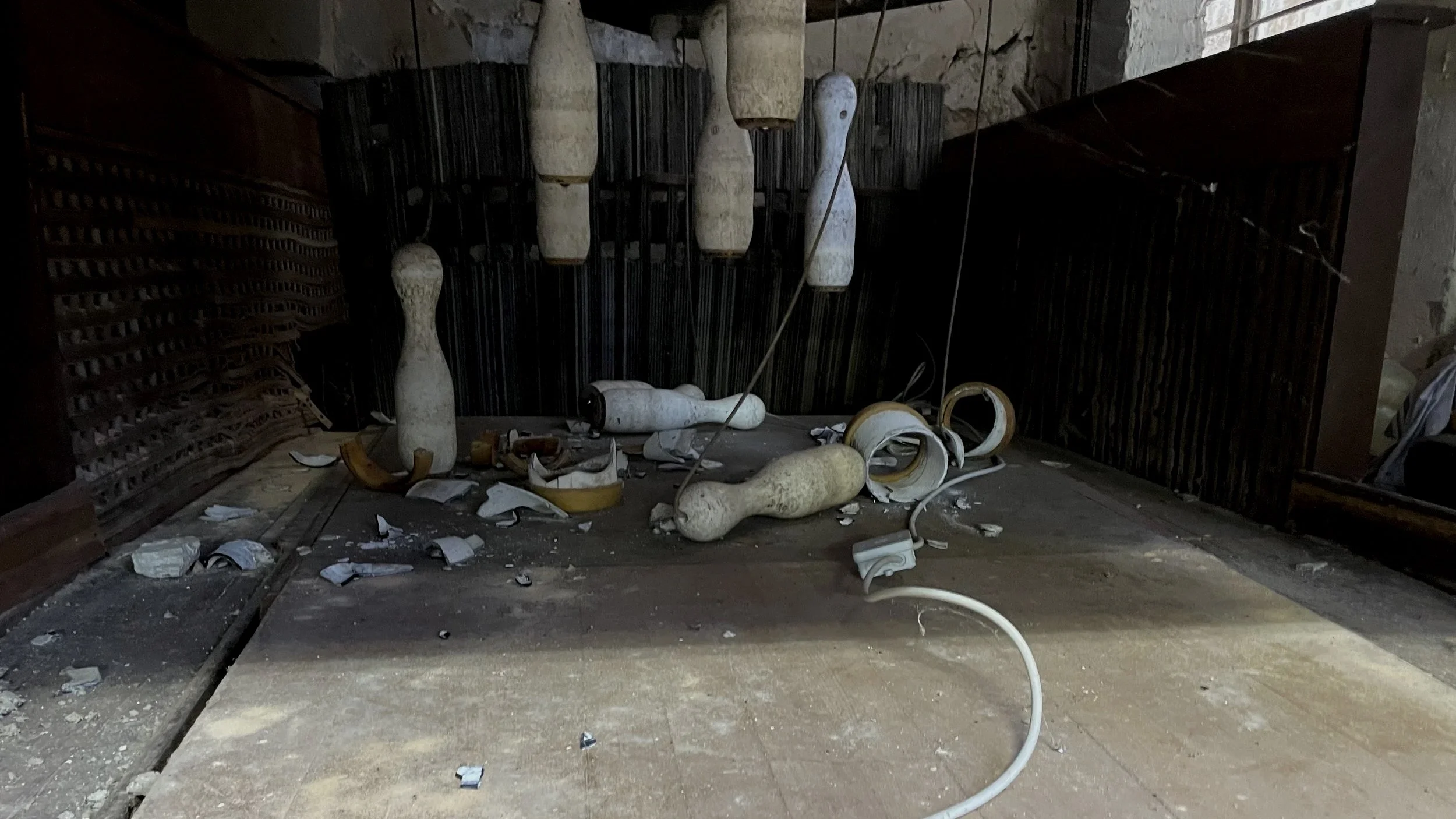 Ein Zimmer mit zerbrochenen Gegenständen und Müll auf dem Boden, darunter Kabel, zerbrochene Keramiken und Staub, mit dunklem Hintergrund.