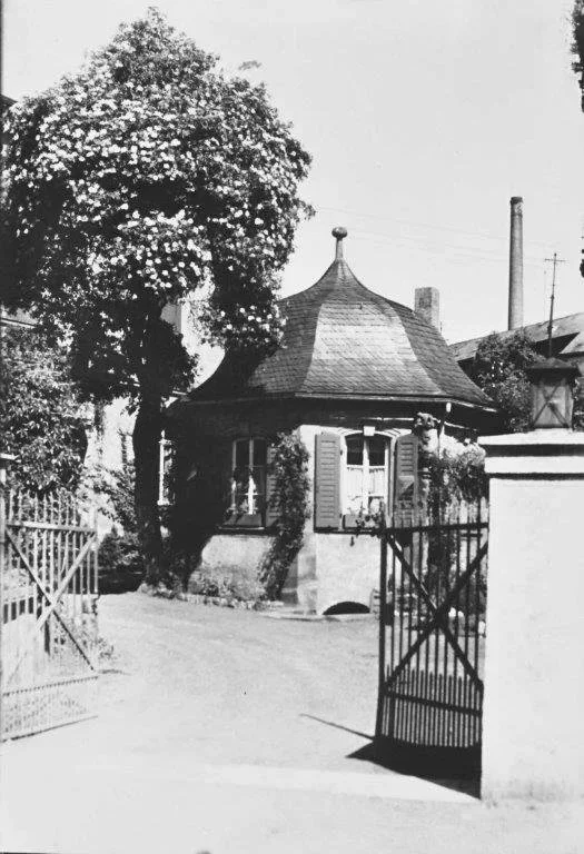 Ein altes Haus mit runder Dach und offenen Fenstern, umgeben von einem Garten mit einem Zäun.