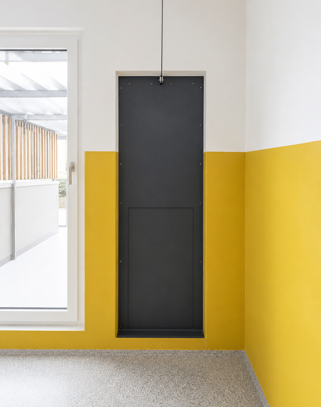 Blick auf einen dunklen Schrank in einer weißen und gelben Wand mit einem Glas- oder Kunststofffenster rechts davon, das auf eine Terrasse oder einen Balkon führt.