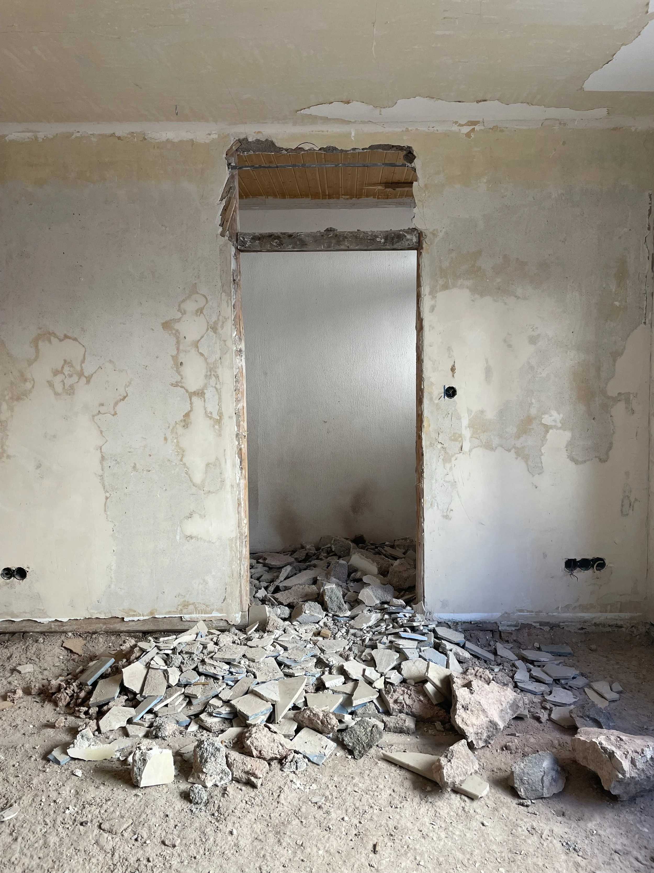 Innenraum eines Raumes mit teilweise abgerissener Wand und vielen Steinen auf dem Boden, Umbauarbeiten im Gange.