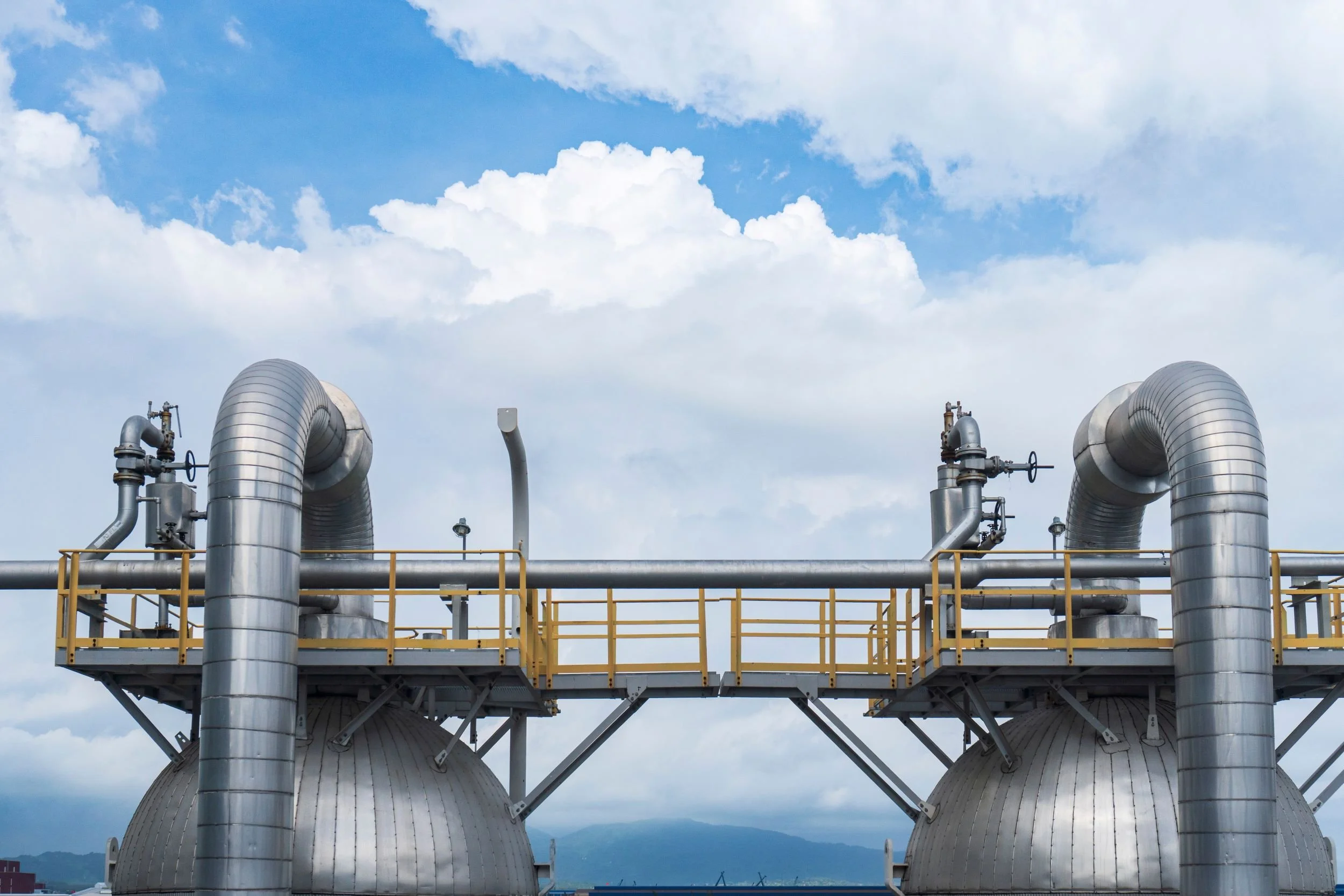 Großtechnische, isolierte Prozessbehälter mit dicken Rohrleitungen und gelben Laufstegen in einer Gas- und Chemieanlage vor blauem Himmel