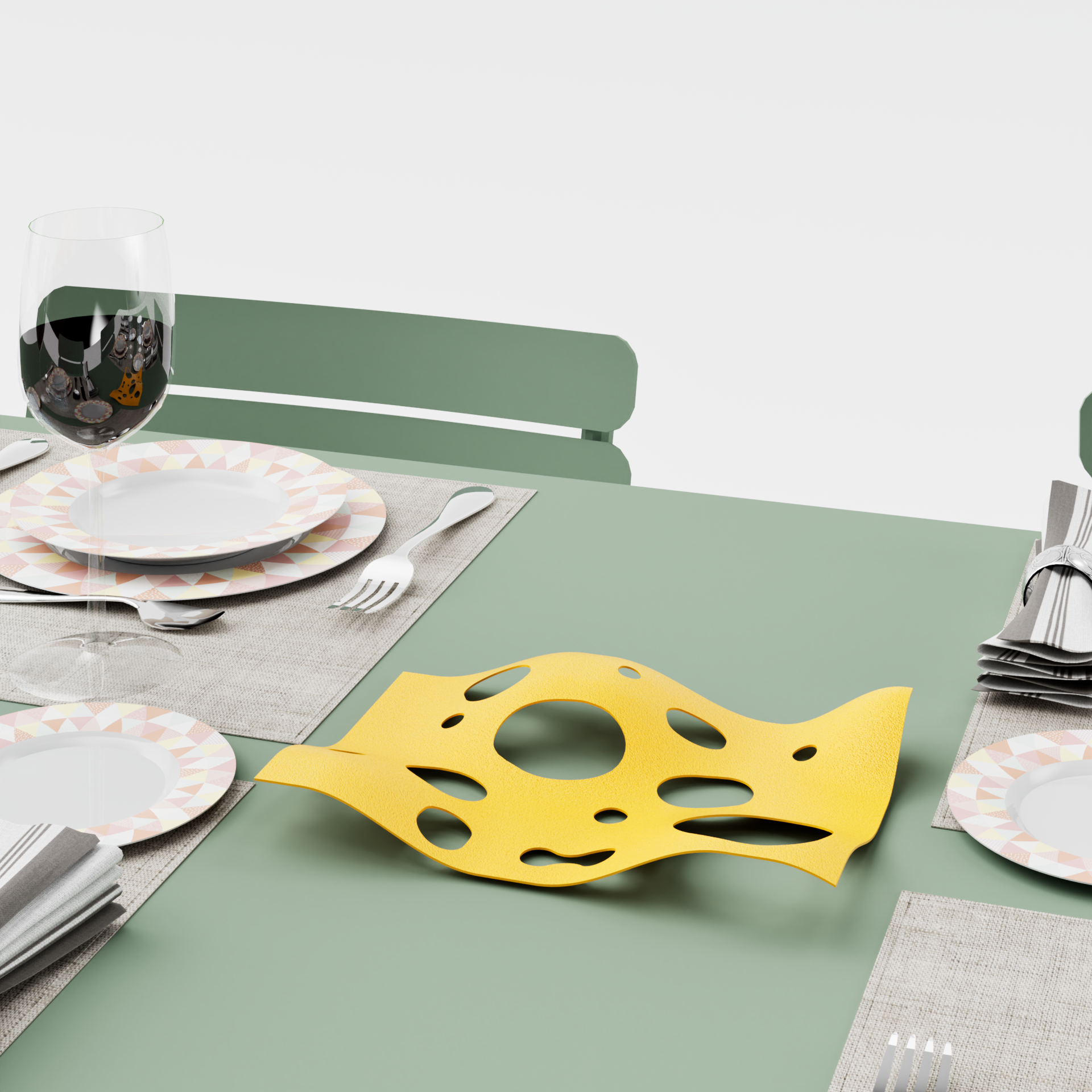 Table verte avec assiettes, verre de vin rouge, fourchette et cuillère, nappe beige, décoration de fromage en plastique jaune.