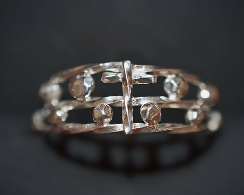 Bague en métal argenté avec des pierres précieuses transparentes, posée sur un fond sombre.