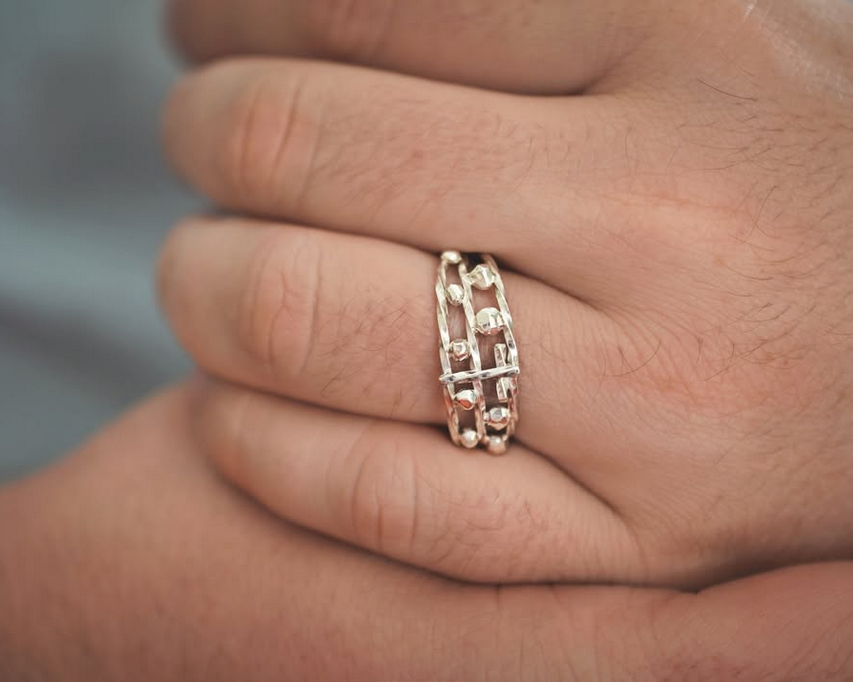 Une main portant une bague en or rose avec un design ouvert et orné de petits diamants.