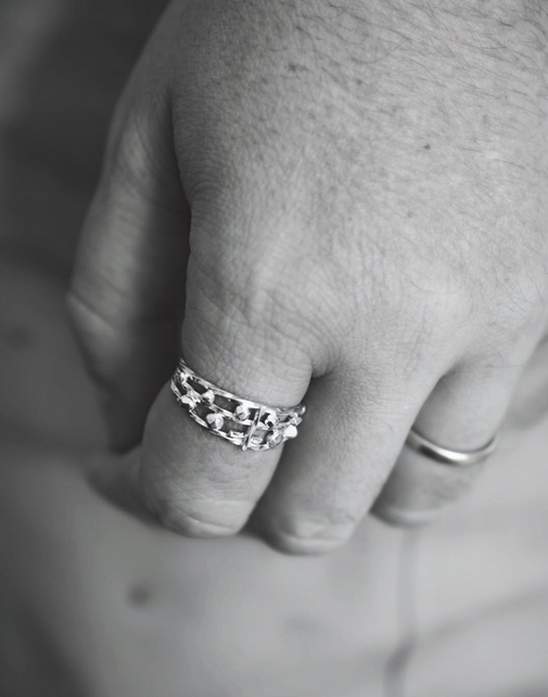 Main d'homme portant une bague en argent à l'index et une autre à l'annulaire, en noir et blanc.
