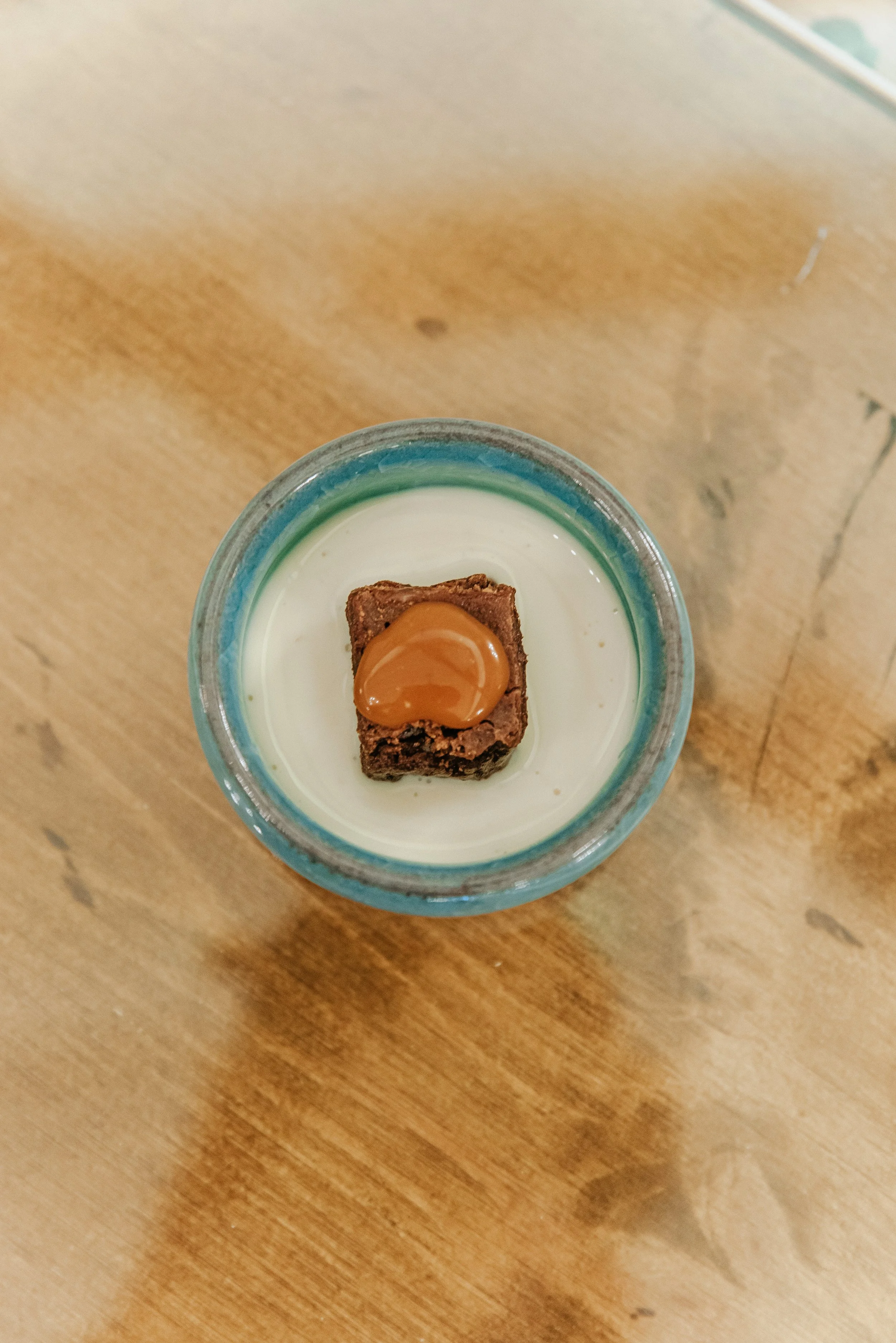 Vaso de cristal con leche y un trozo de pastel de chocolate decorado con caramelo.