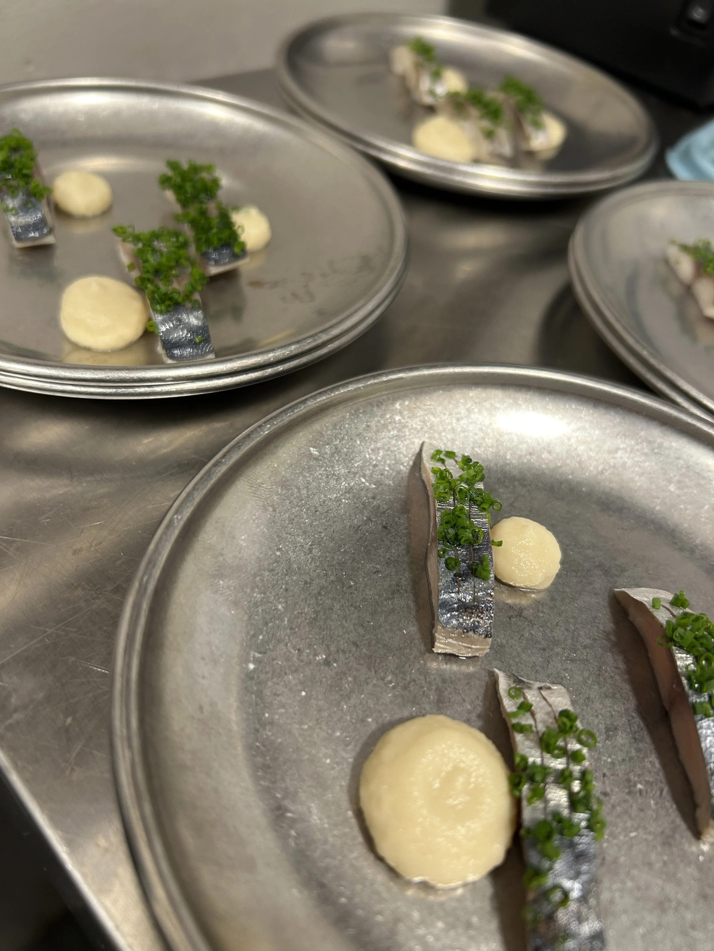 Platos de comida con pescado, patatas y cebollín picado, en platillos de metal en una cocina.