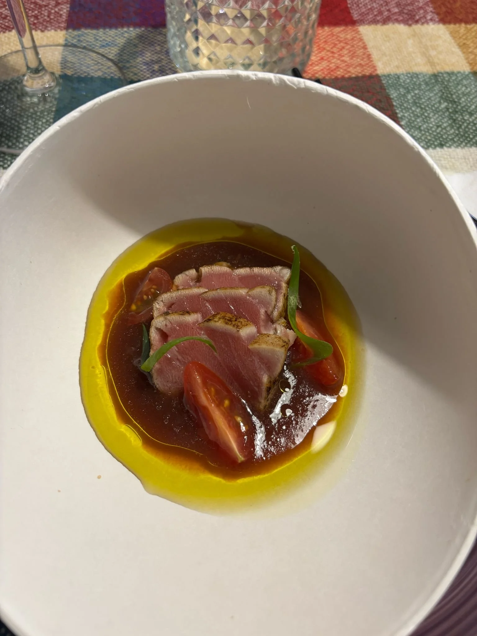 Plato de atún sellado en salsa, decorado con cebollines y tomate, en un plato blanco, en una mesa con mantel de cuadros.