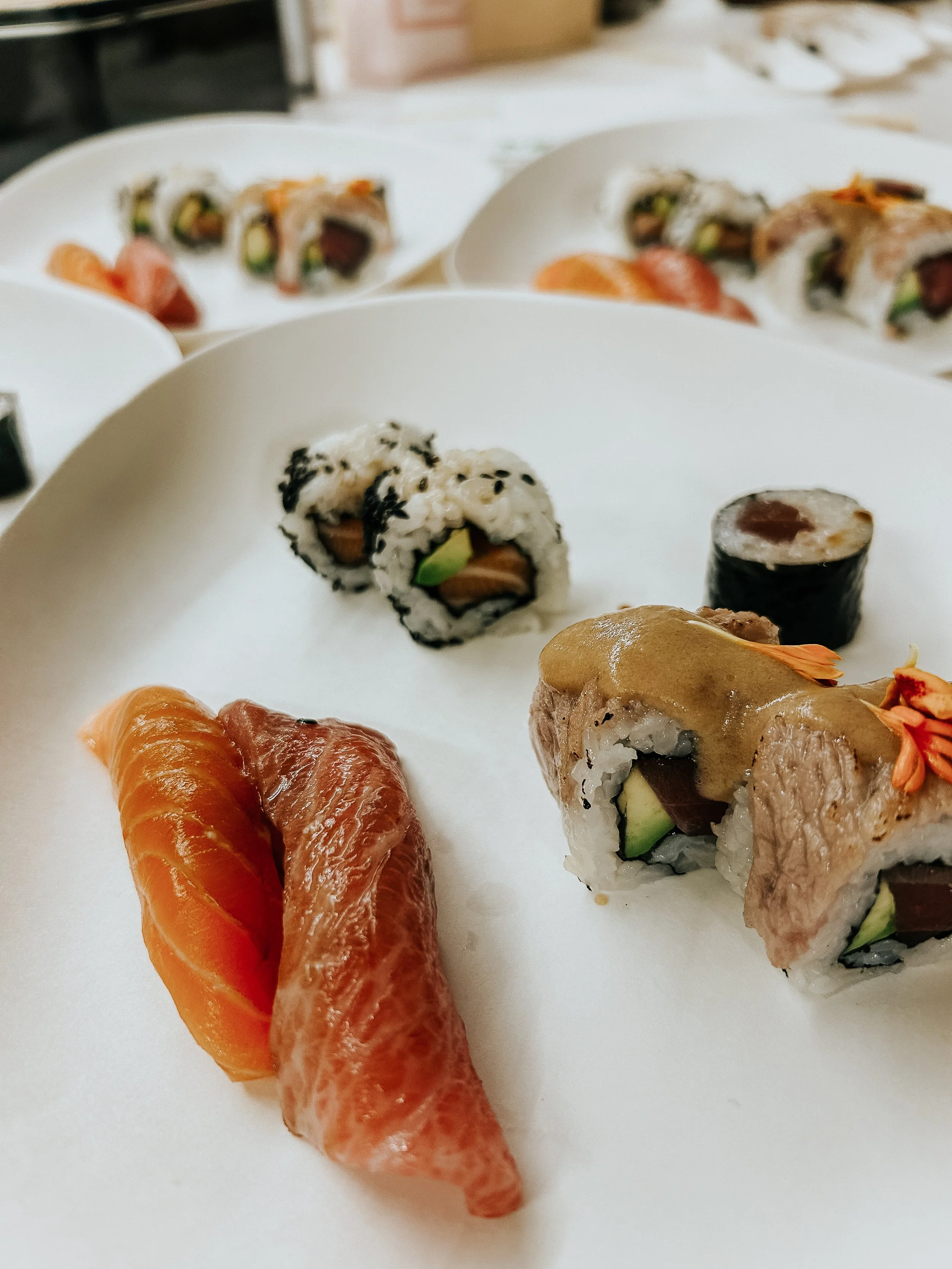 Variedad de sushi con salmón, atun, aguacate y otros ingredientes en platos blancos.