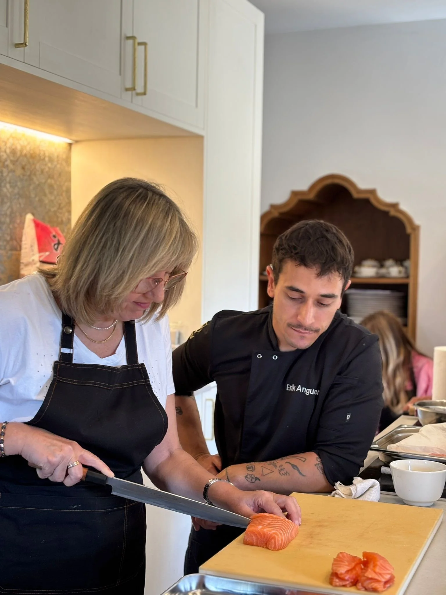 Dos personas cocinando en una cocina, cortando salmón en una tabla de madera.
