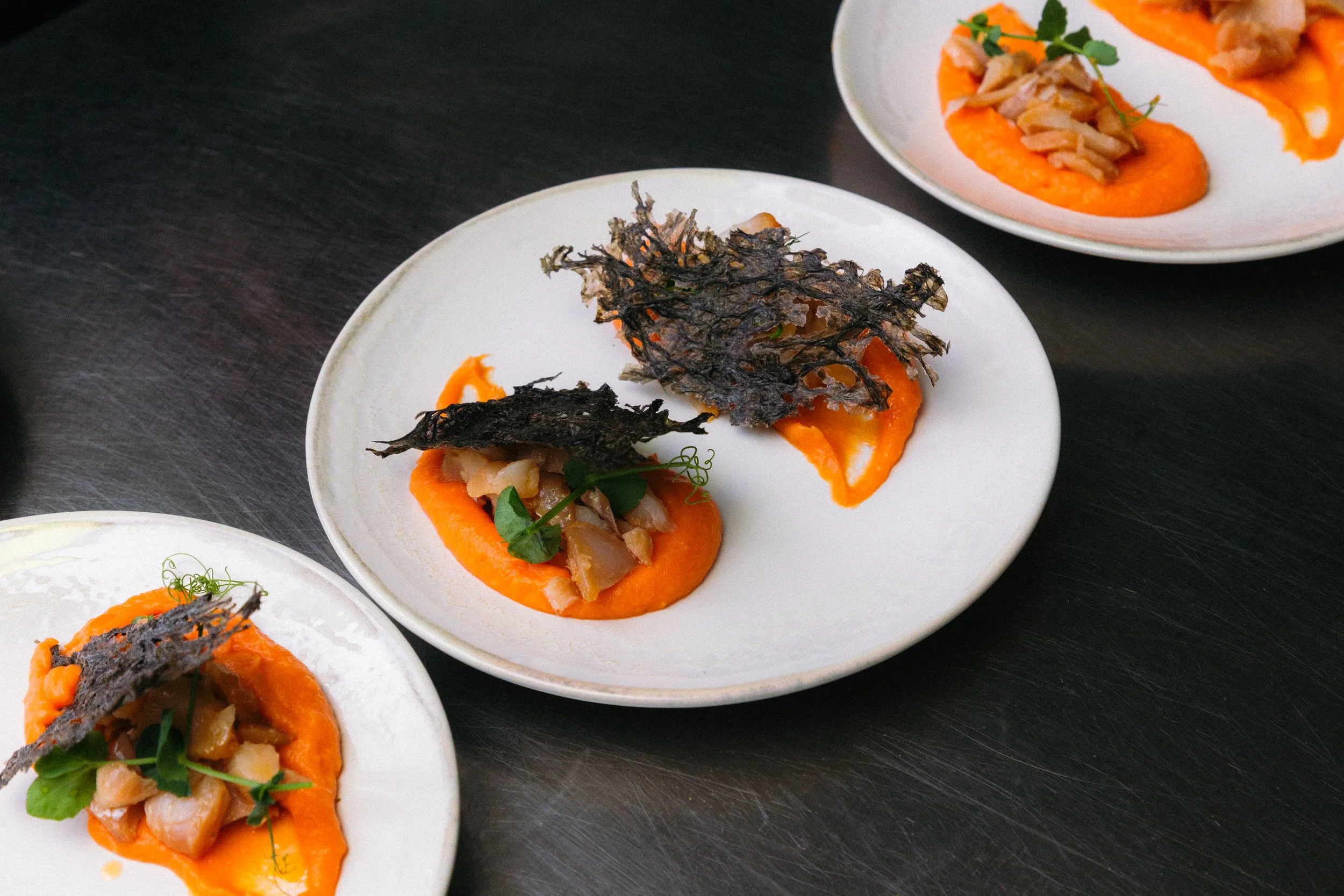 Platos pequeños con puré de zanahoria, carne y algas comestibles en diferentes presentaciones.