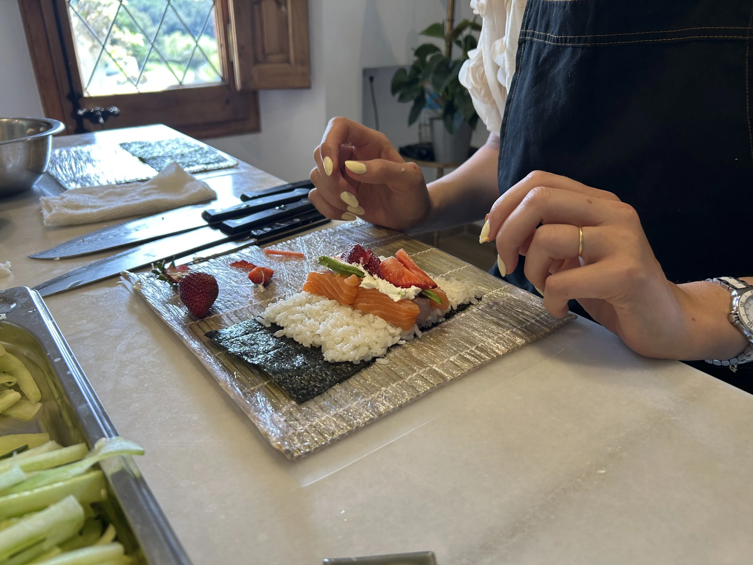 Persona haciendo sushi con ingredientes frescos en una cocina luminosa.
