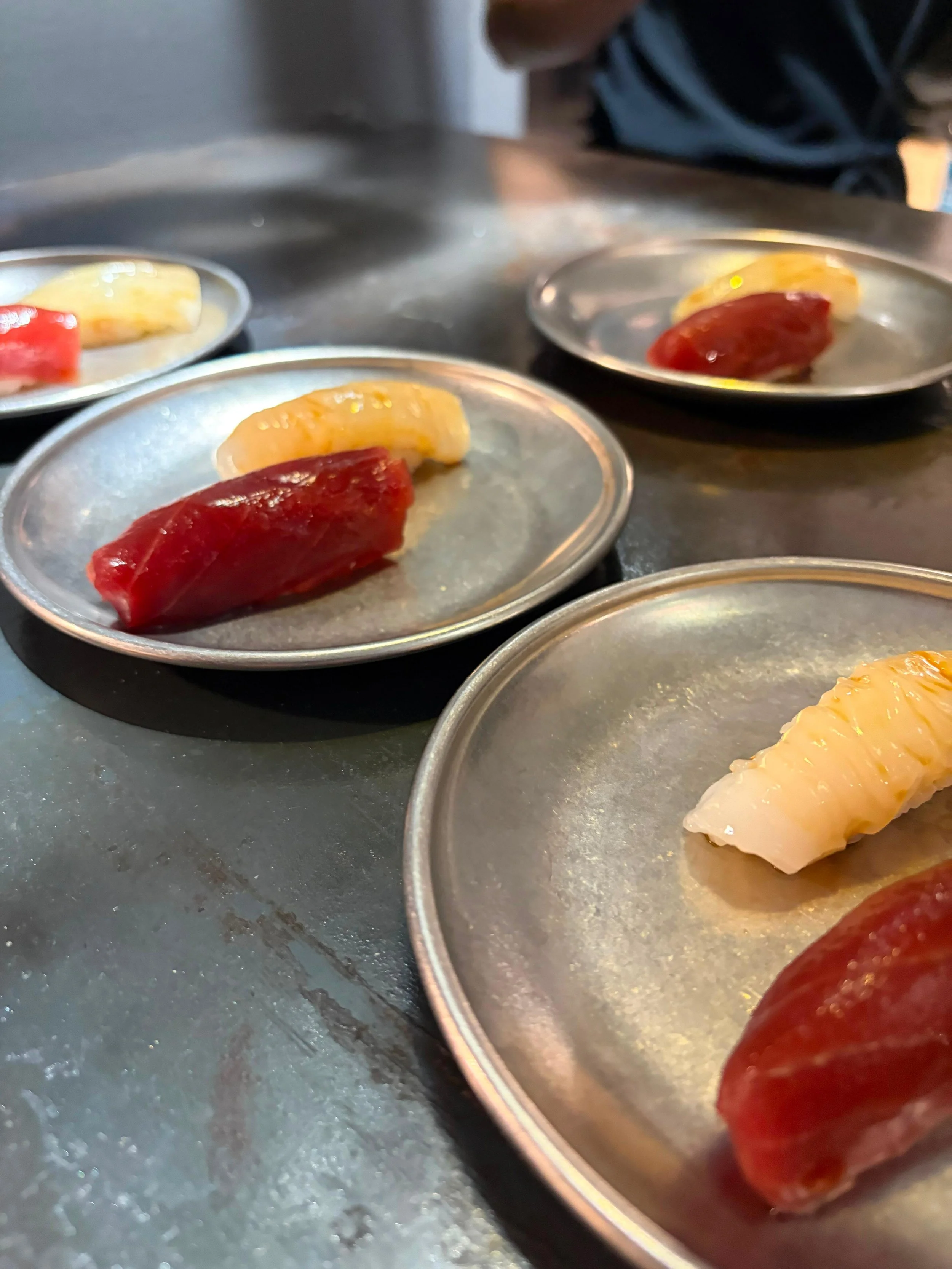 Trozos de sushi con pescado en platos de metal sobre una superficie de cocina.