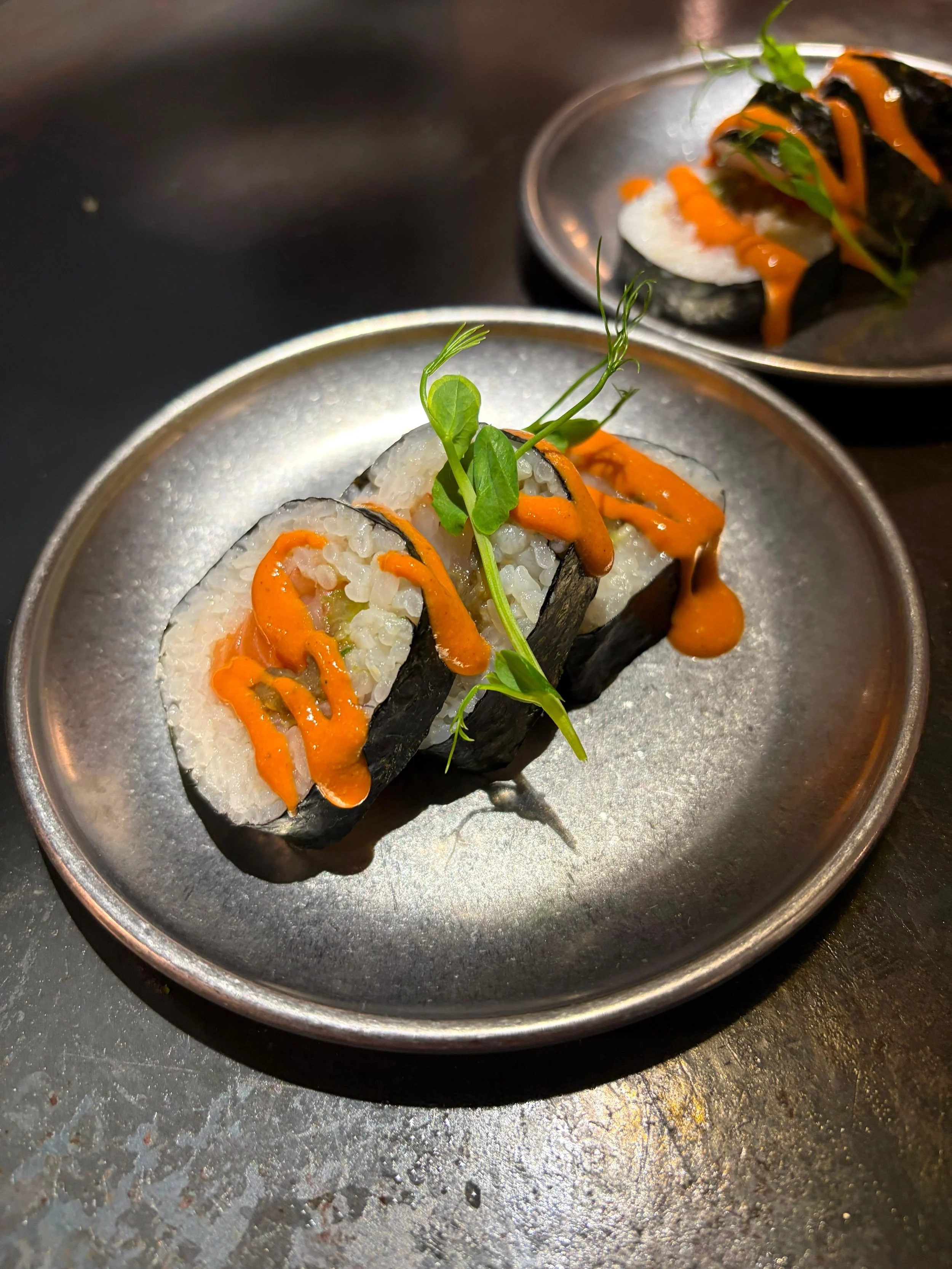 Rollos de sushi con alga nori, arroz, envoltura de salmón, y decorados con salsa naranja y vegetación.
