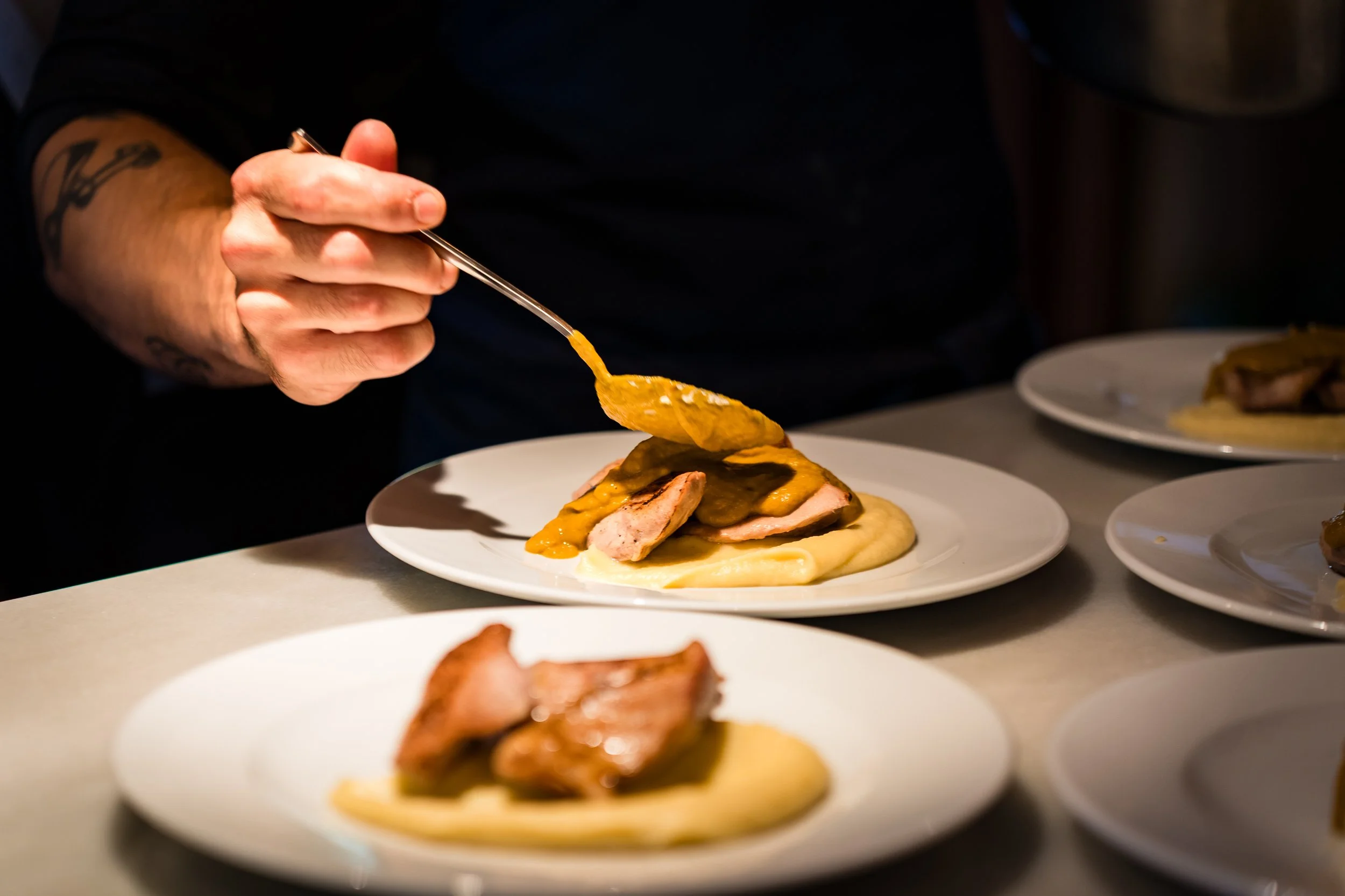 Persona sirviendo comida en un plato con salsa en un servicio de catering. Catering mediterráneo. Catering para empresas.