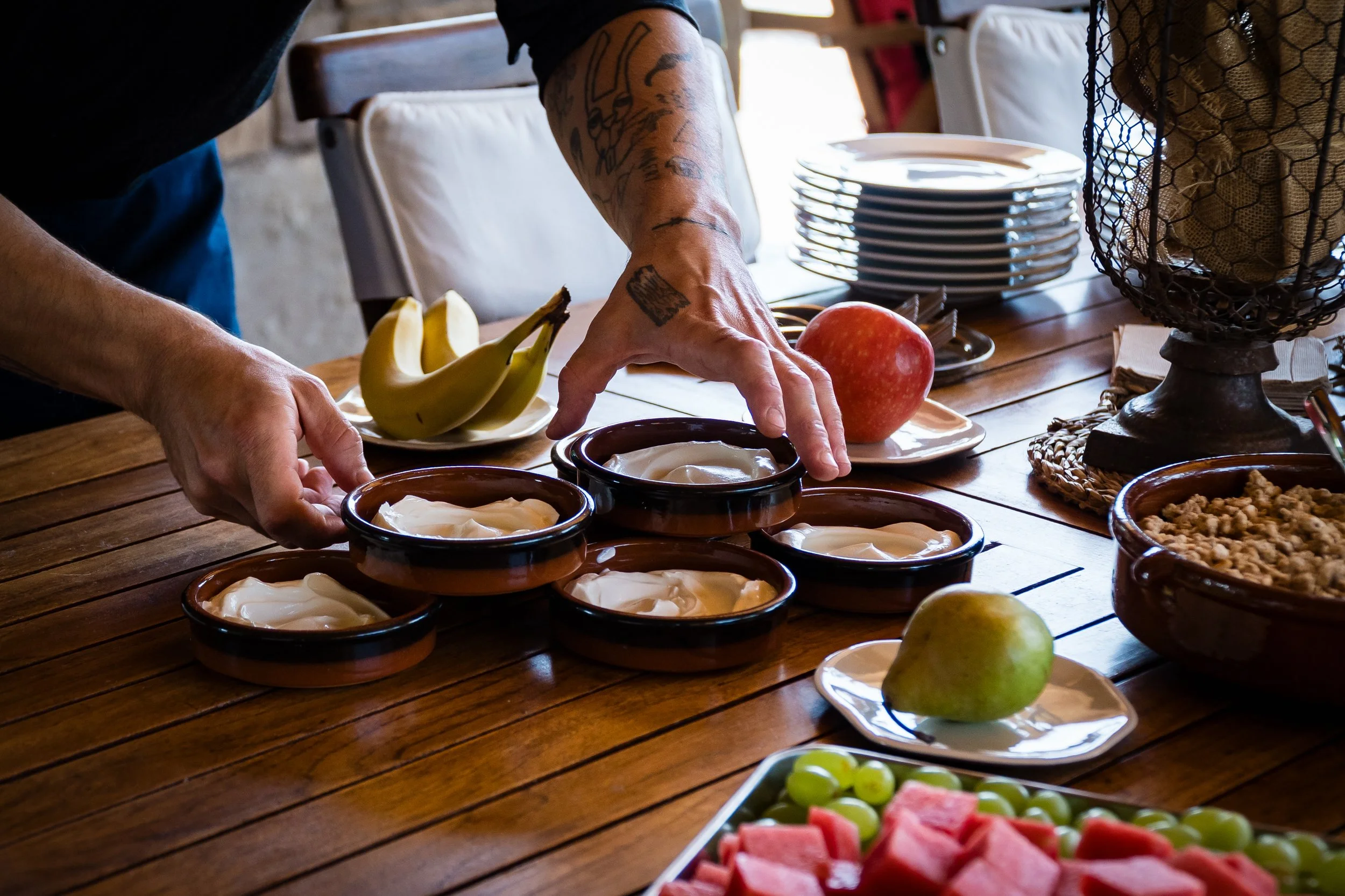Persona colocando yogurt en recipientes en una mesa con frutas y platos