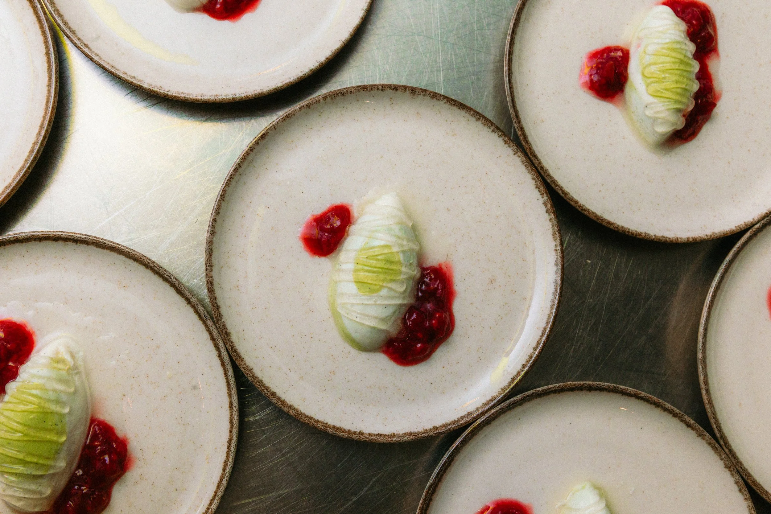 Porciones de postre con una base de crema o mousse blanca, decoradas con crema, frutos rojos y salsa de frutos rojos en platos de cerámica beige con borde marrón.