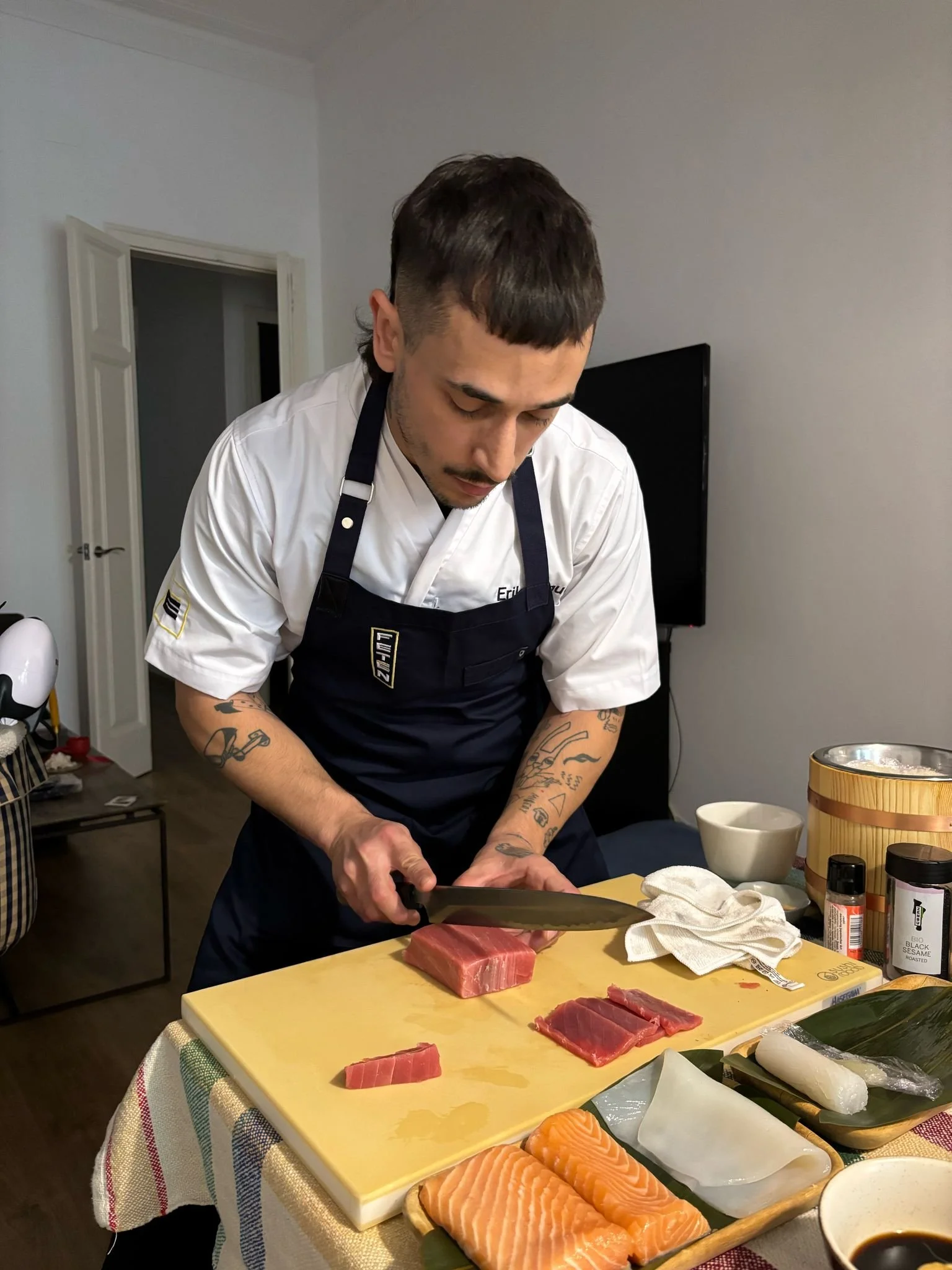 Hombre cocinero preparando pescado en la mesa con ingredientes como salmón, y utensilios de cocina.