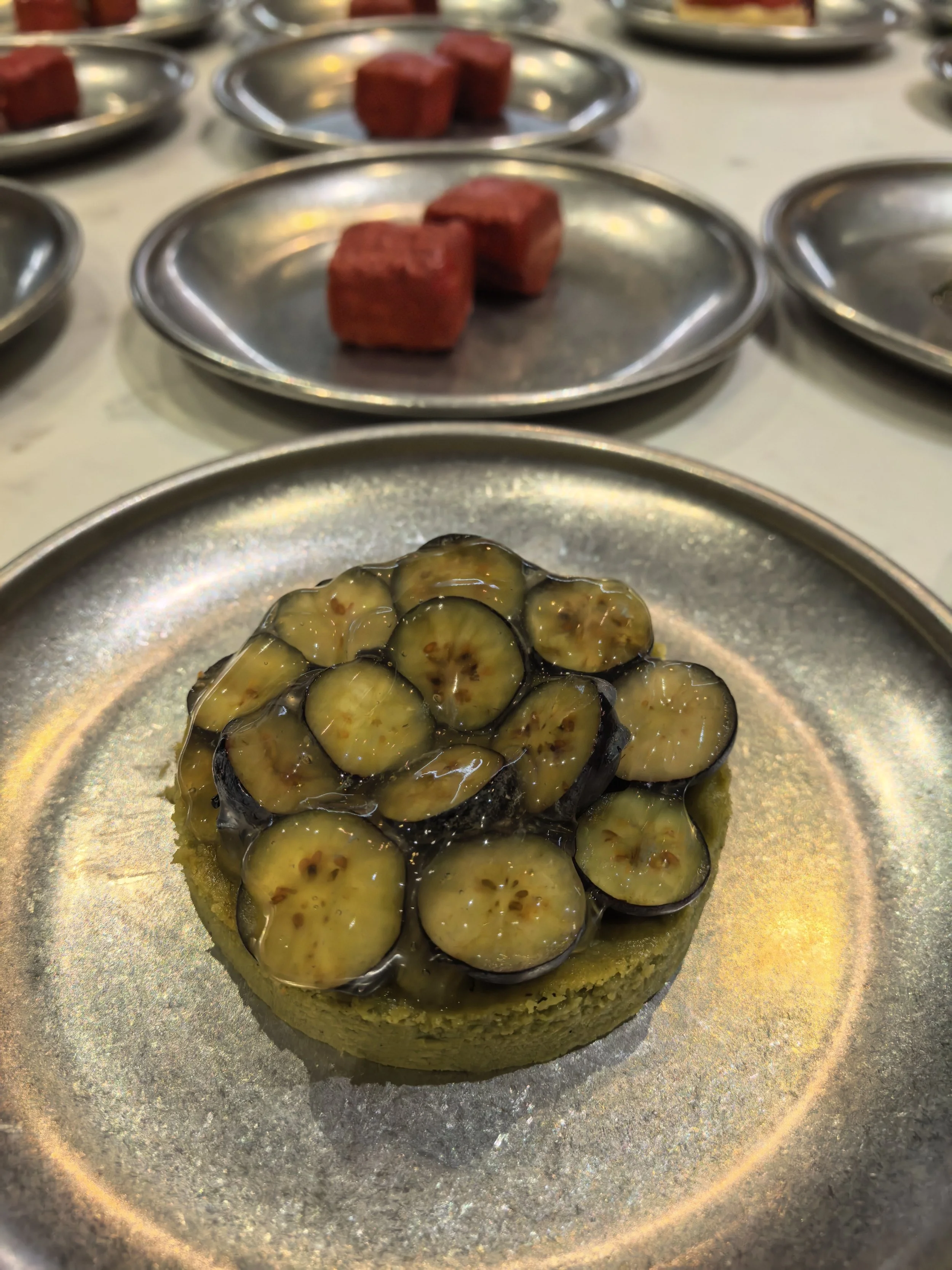 Un postre con base de queso decorado con rodajas de kiwi cubiertas en azúcar en un plato plateado.