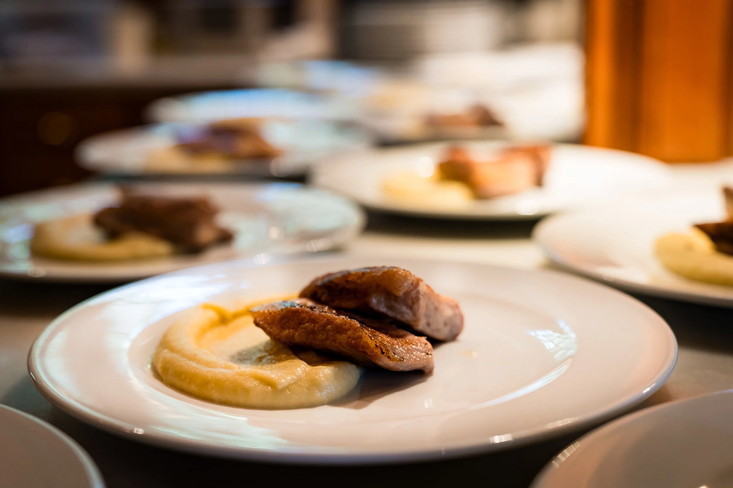 Platos con diferentes tipos de carnes y puré de chirivía en una mesa, en un ambiente de restaurante.