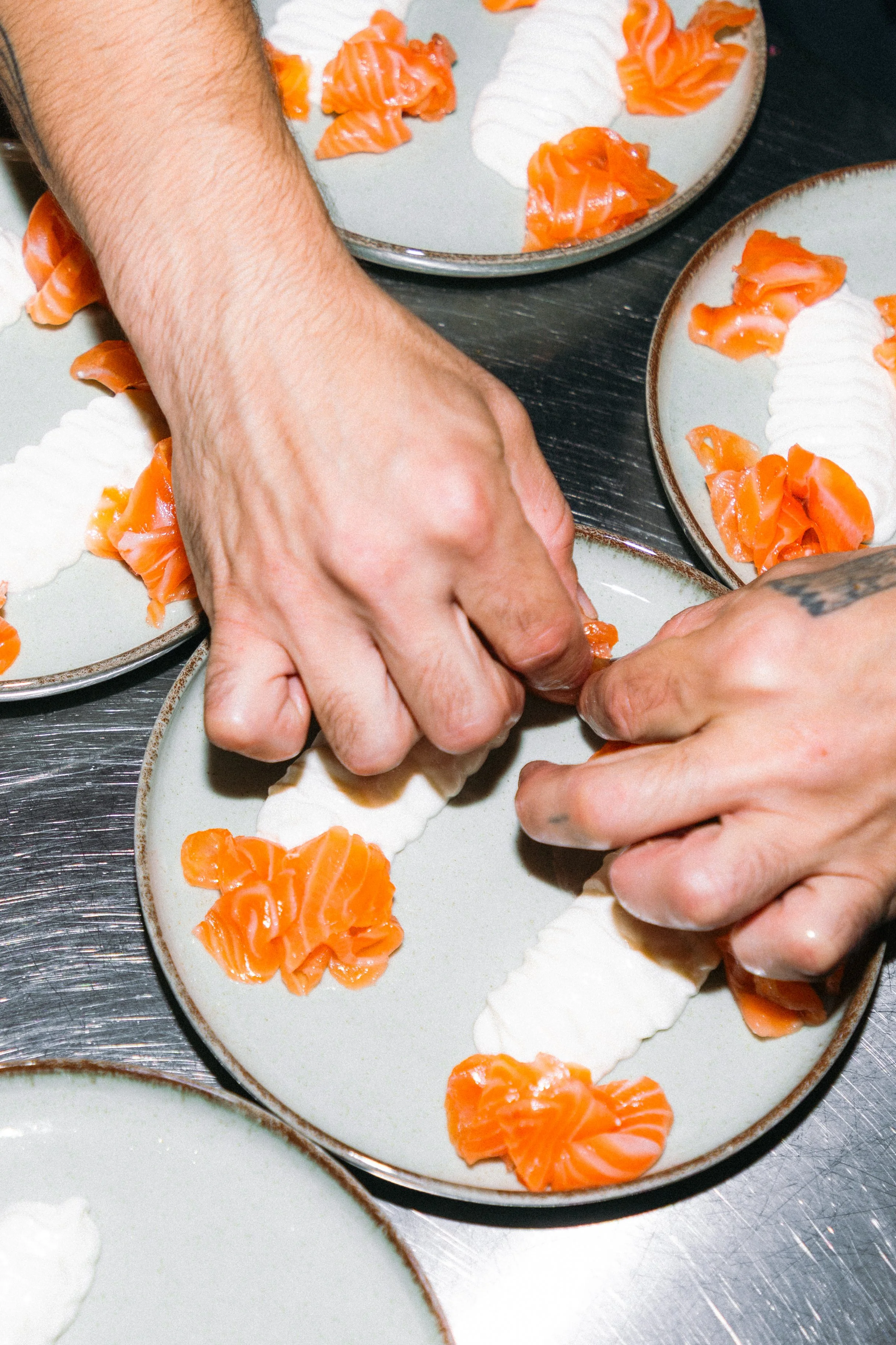 Manos preparando rollos de sushi con salmón en platos blancos decorados con salmón y arroz.
