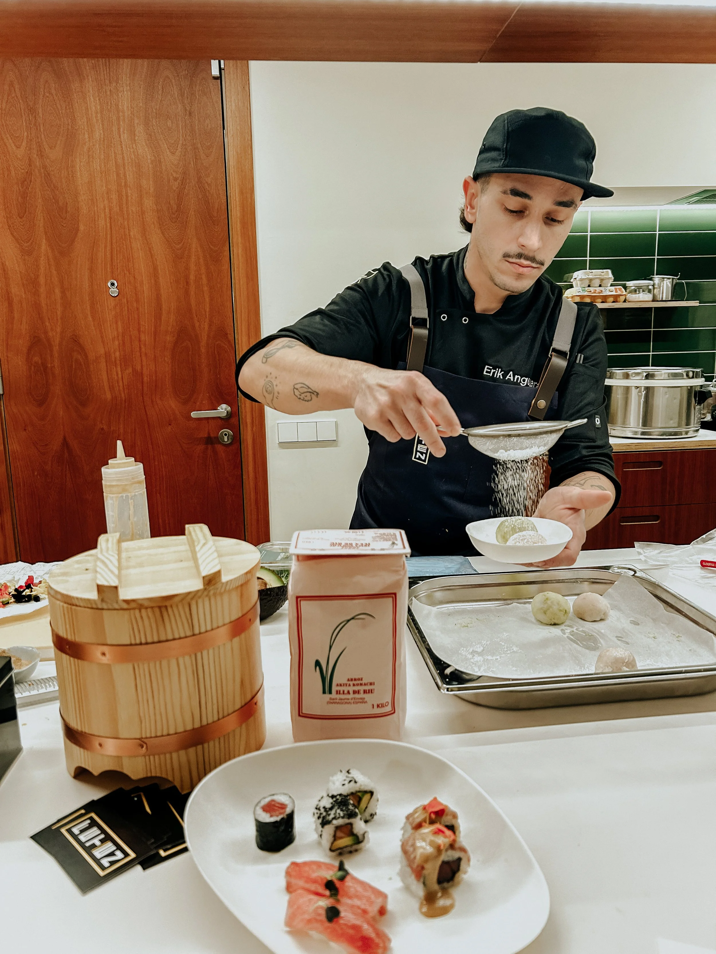 Hombre preparando sushi en la cocina, con ingredientes y utensilios sobre la mesa.