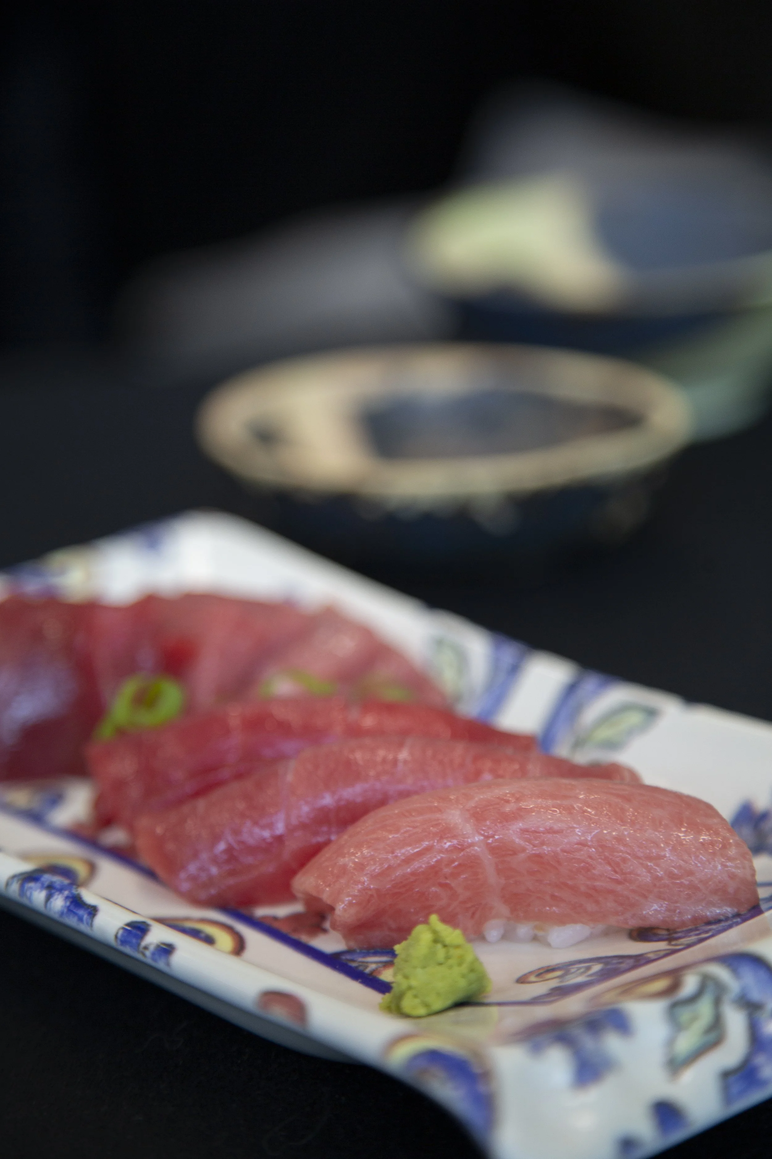 Trozos de sashimi de atún en un plato decorativo con un poco de wasabi al lado.