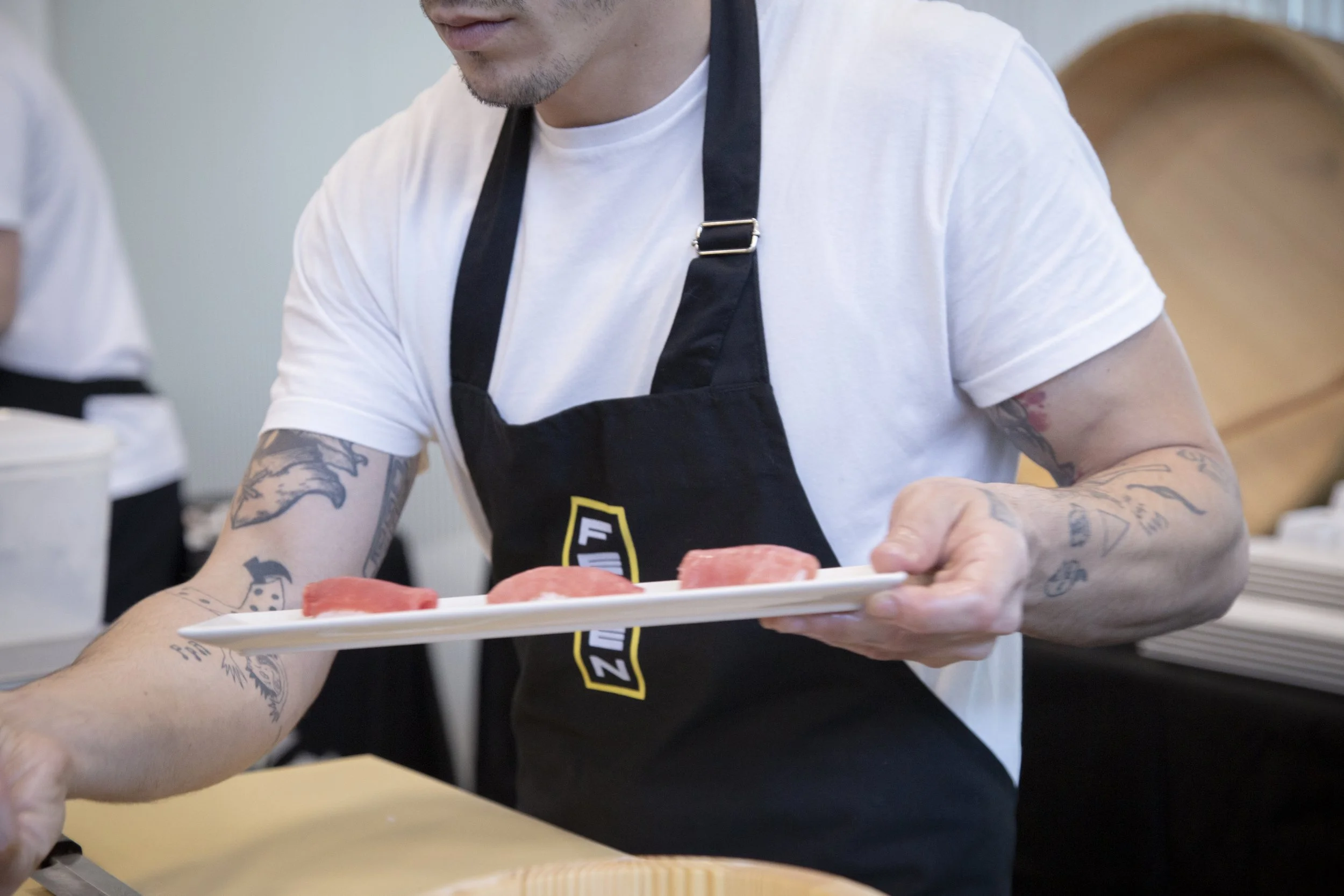 Persona sirviendo rodajas de carne en un plato, usando un delantal negro en un ambiente de cocina o restaurante.