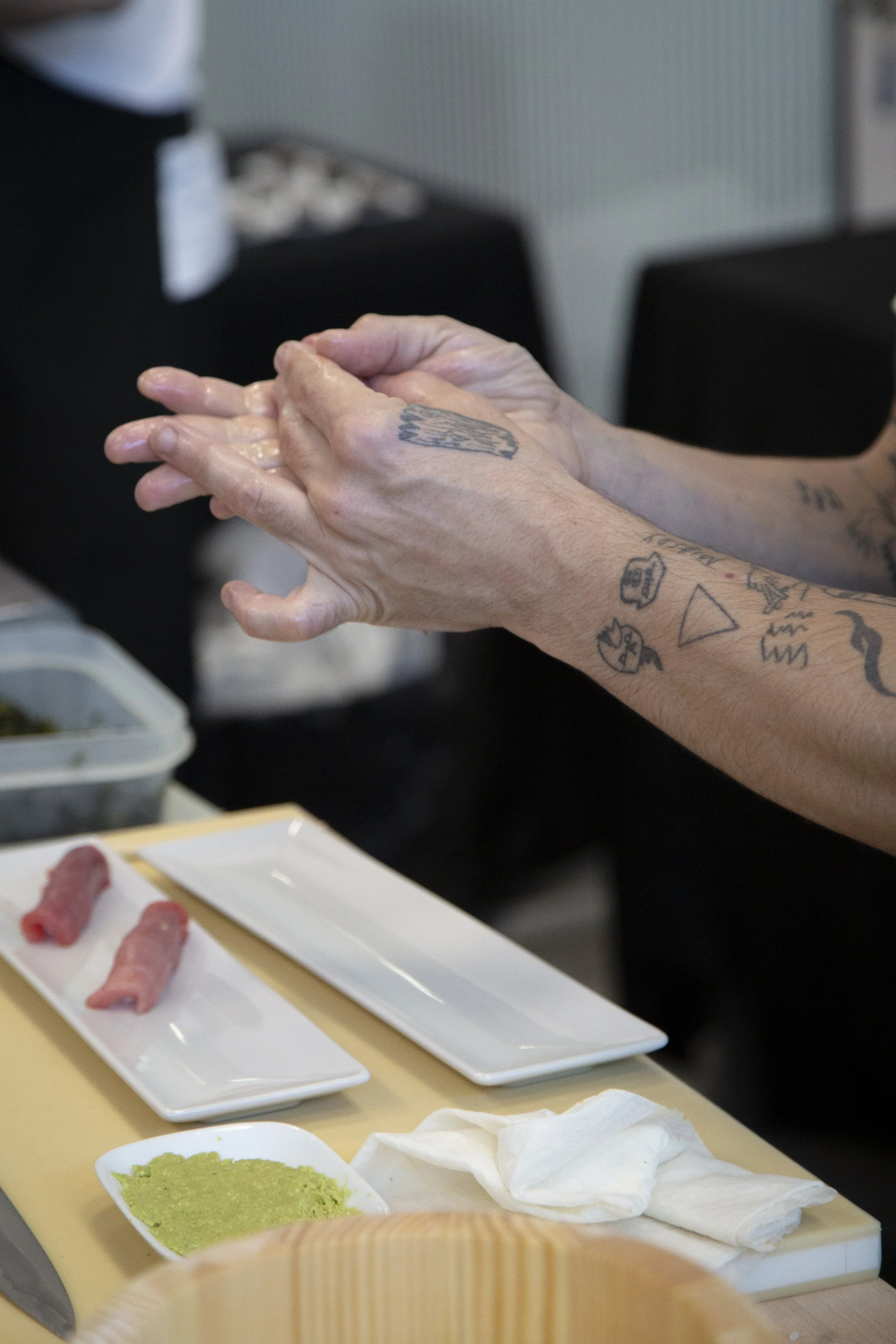 Personas preparando sushi con wasabi y arroz en una mesa, con ingredientes y herramientas de cocina.