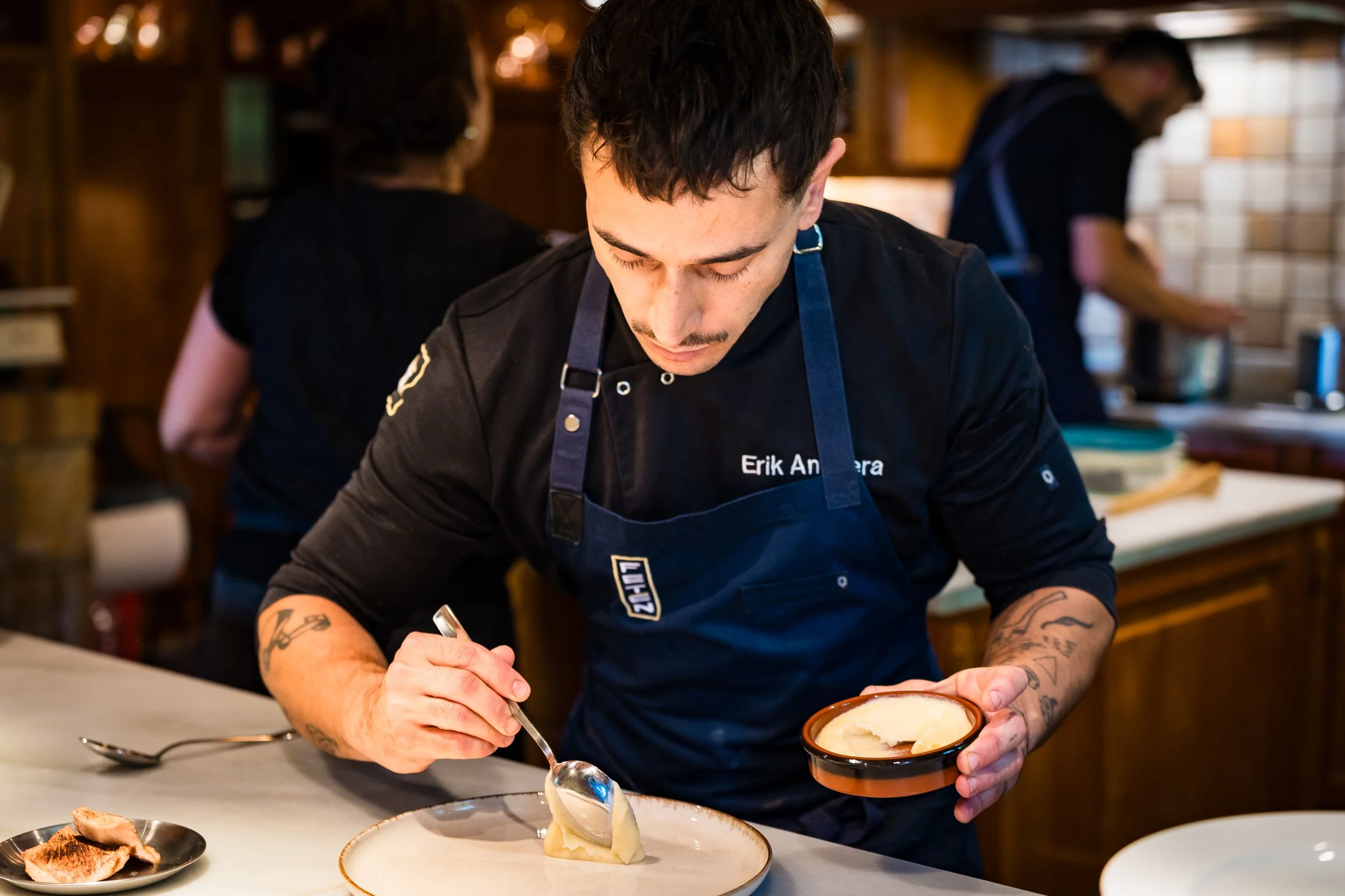 Joven cocinero decorando un platillo con puré en una cocina profesional.