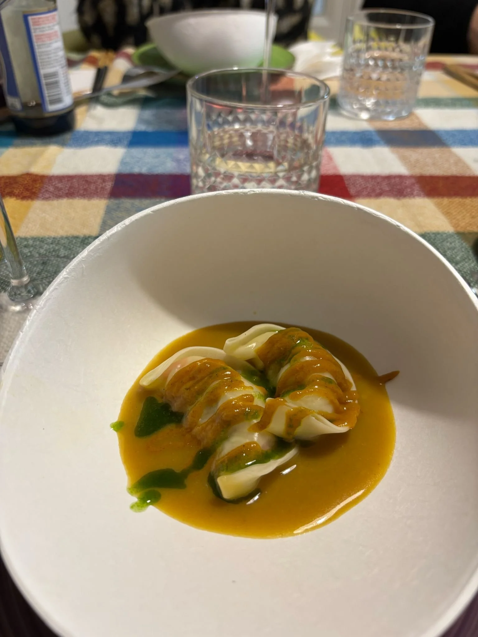 Plato de bolas de masa envueltas en hoja de pasta en salsa amarilla con gotas de aceite y decoración de hierbas, en un plato blanco.