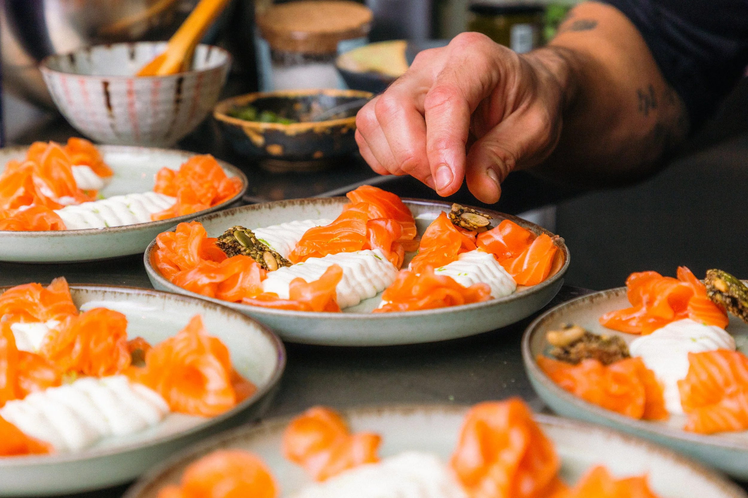 Persona decorando platos con salmón ahumado y queso crema en un mostrador lleno de platos similares.