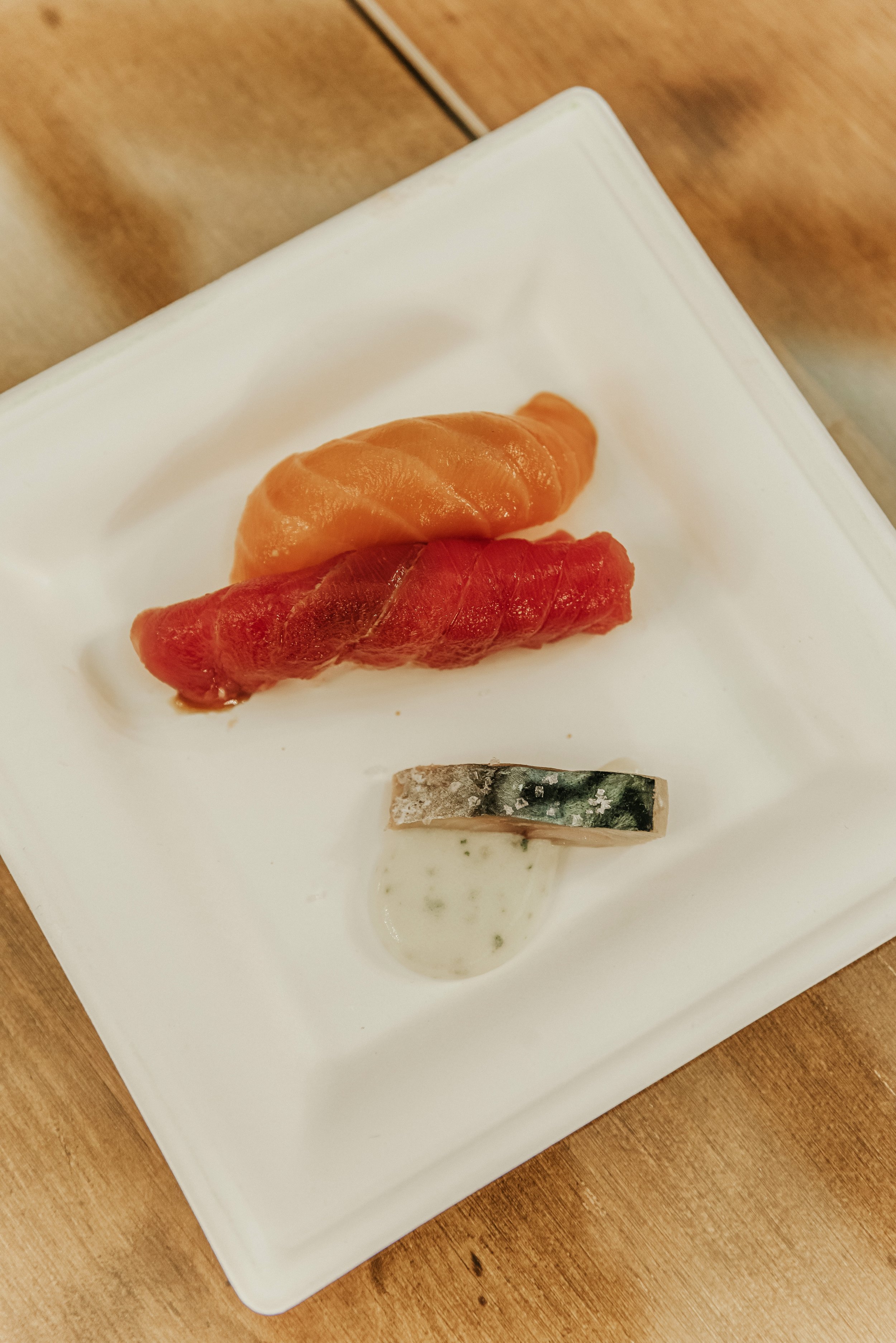 Sushis variados en plato blanco con salsa en una mesa de madera.