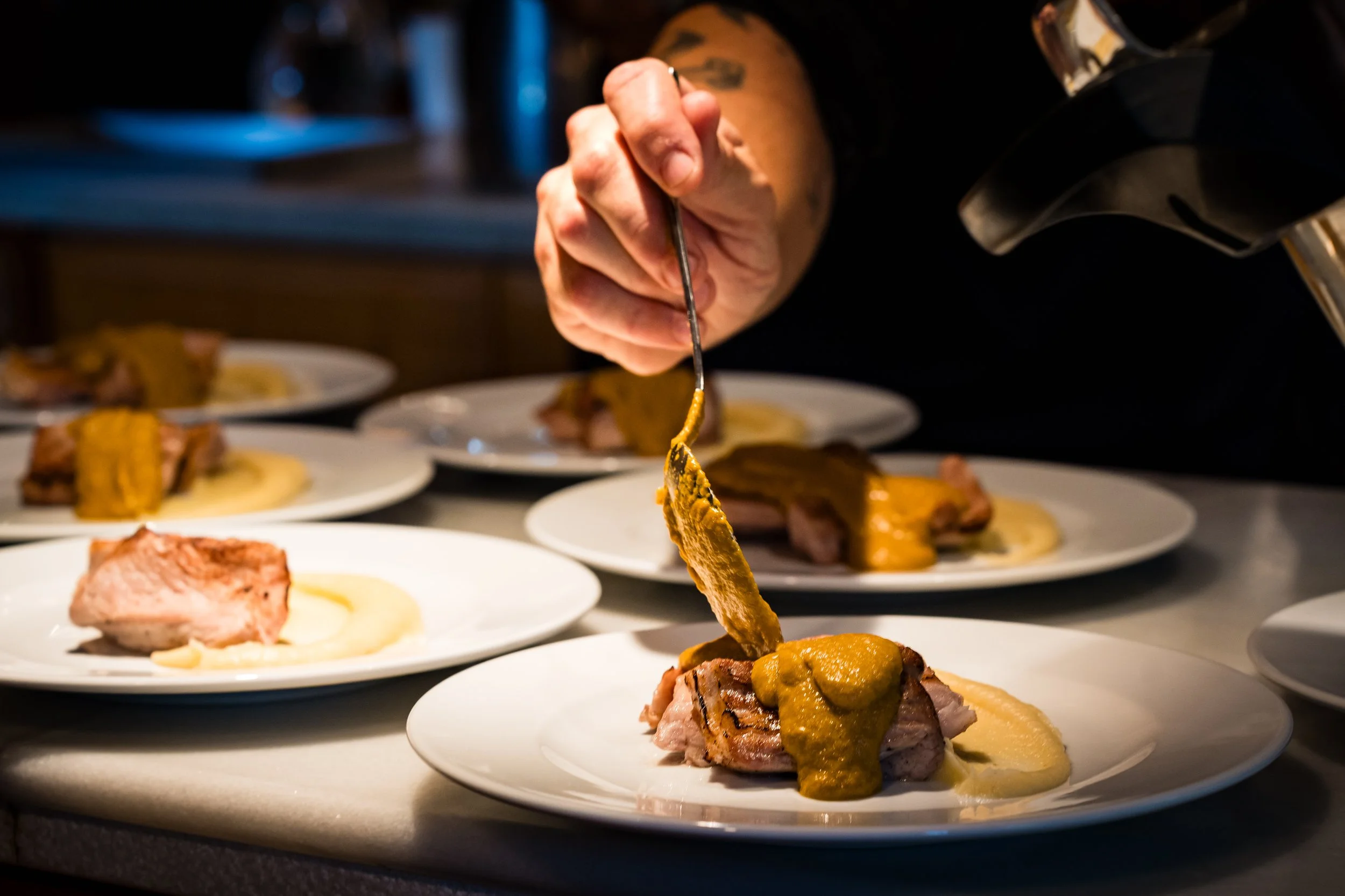 Persona colocando salsa sobre carne en platos blancos con comida en una mesa.