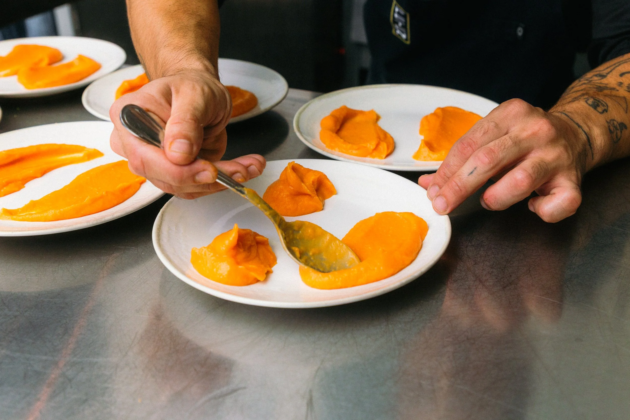 Persona sirviendo puré de calabaza en platos blancos en una cocina.