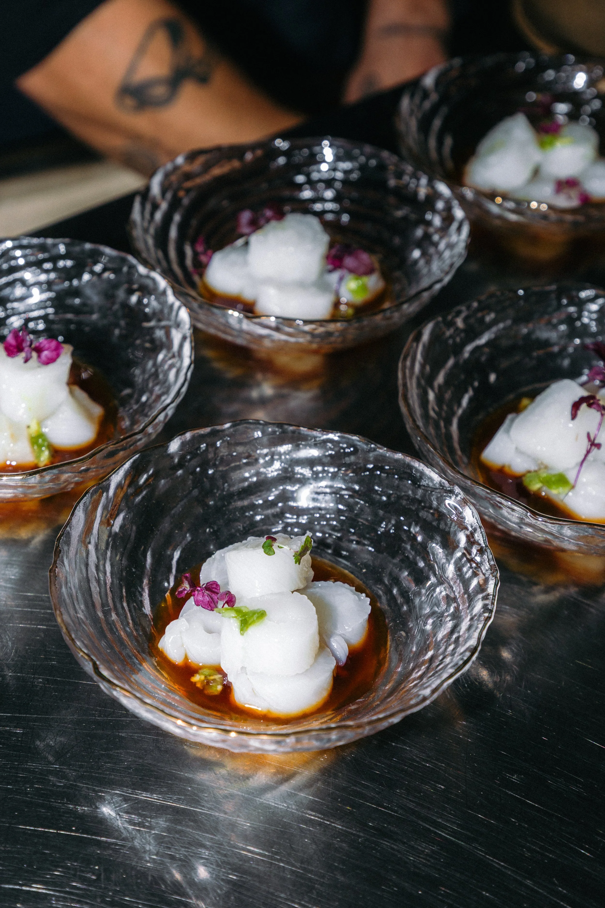 Copas de vidrio elegantes con postre de crema blanca, polvo rosado, y decoraciones de flores pequeñas en una presentación sofisticada.