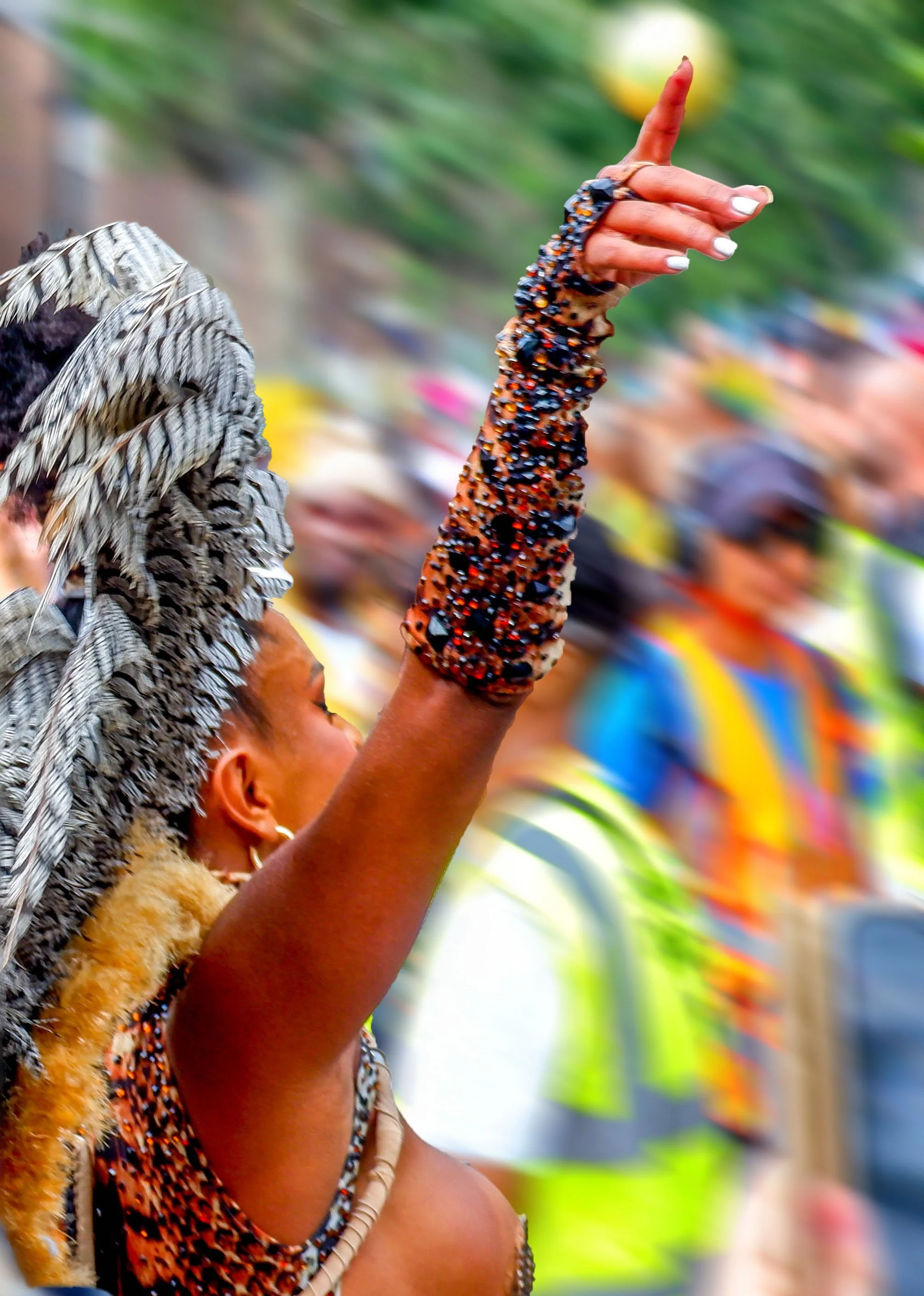 A person wearing traditional, colorful attire with beaded accessories and feathered headgear, raising their arm in a cultural or ceremonial dance.