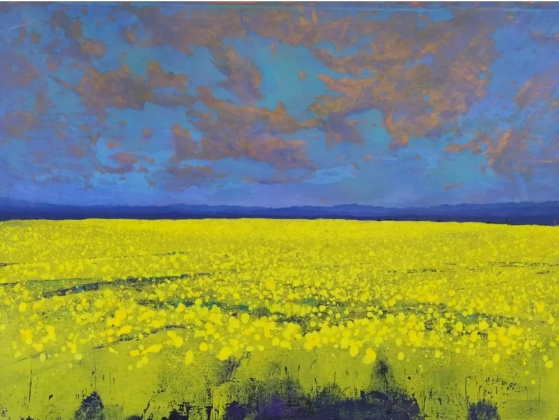 A vibrant painting of a yellow canola field under a blue sky with orange and pink clouds and distant mountains on the horizon.