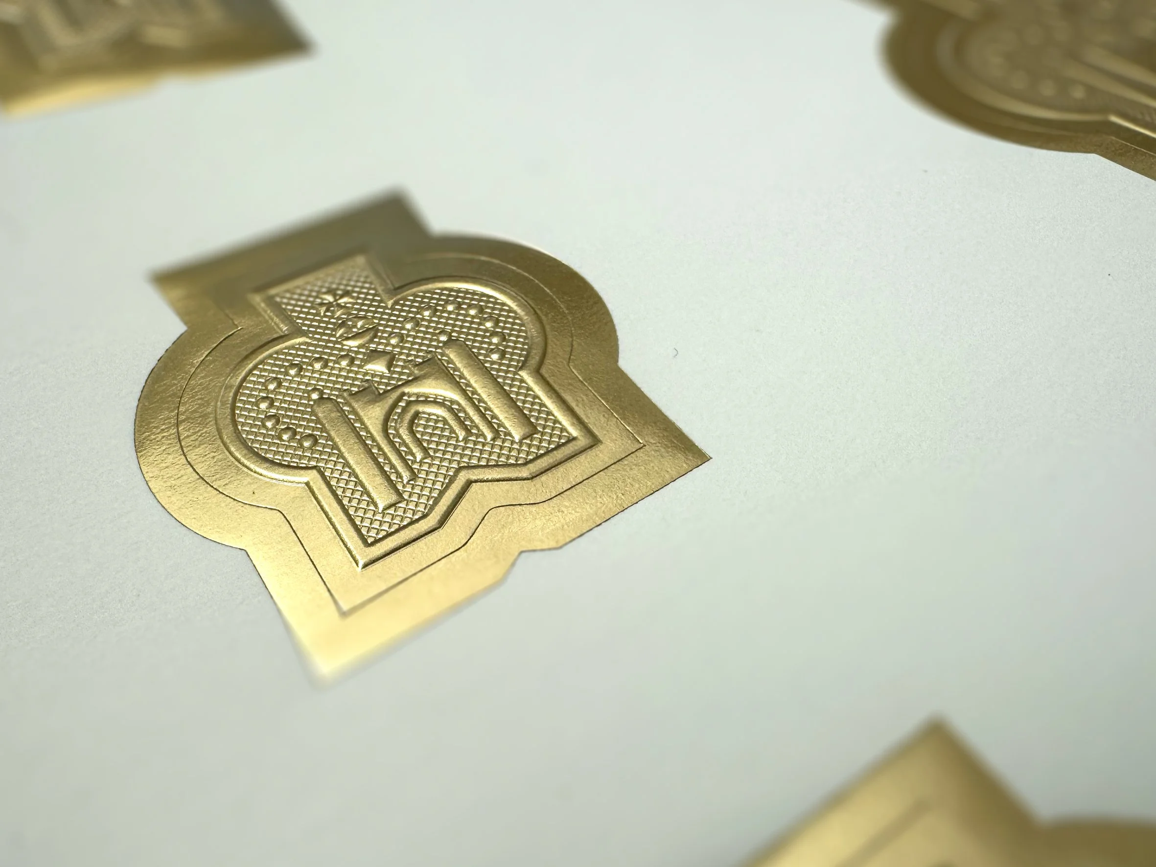 Close-up of gold-colored coins with intricate design and embossed text, scattered on a plain surface.