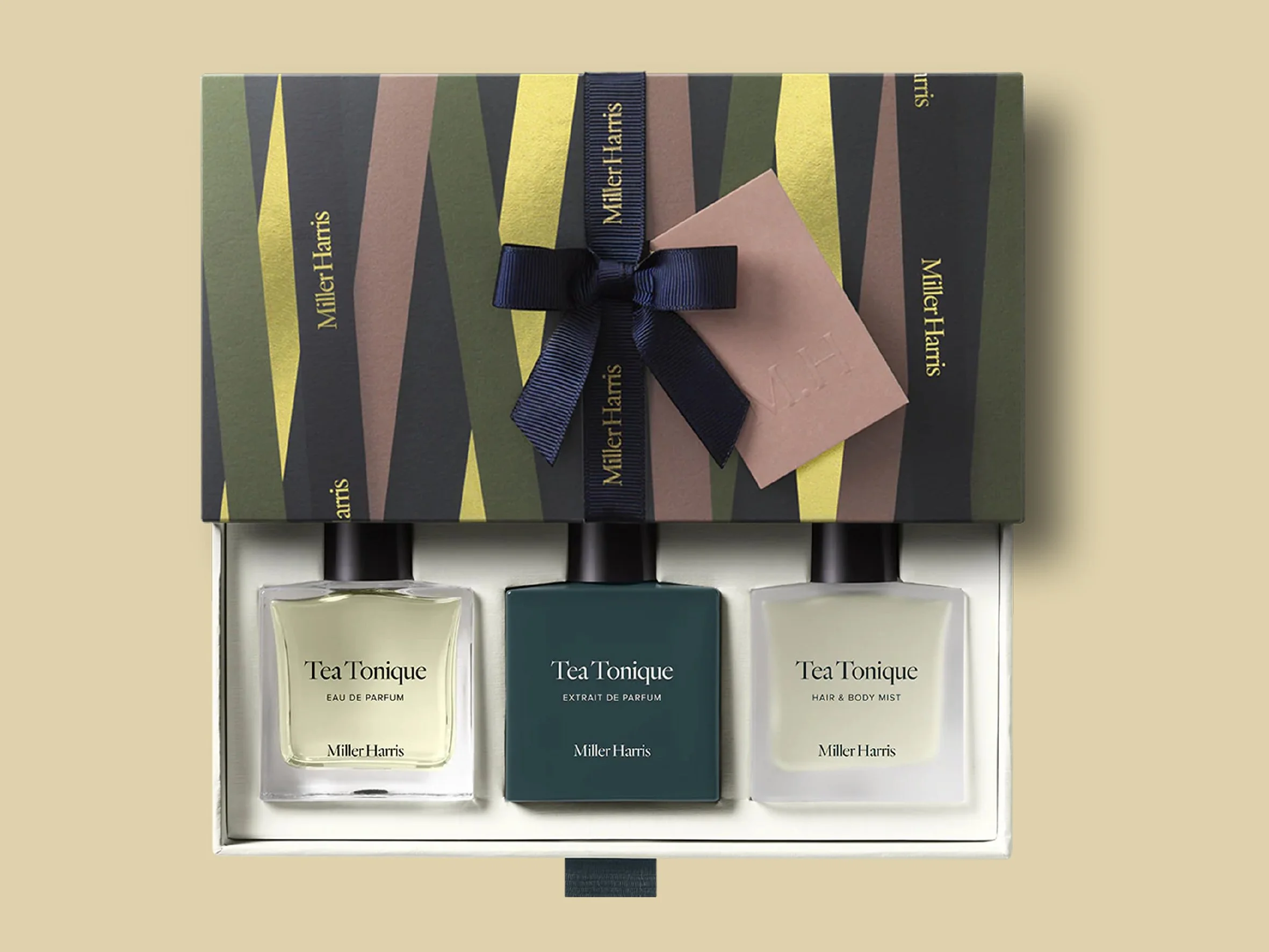A gift box wrapped with a dark grey, green, brown, and yellow abstract patterned paper, tied with a navy ribbon with cold foil litho detailing. Carton packaging produced by Windles Packaging.