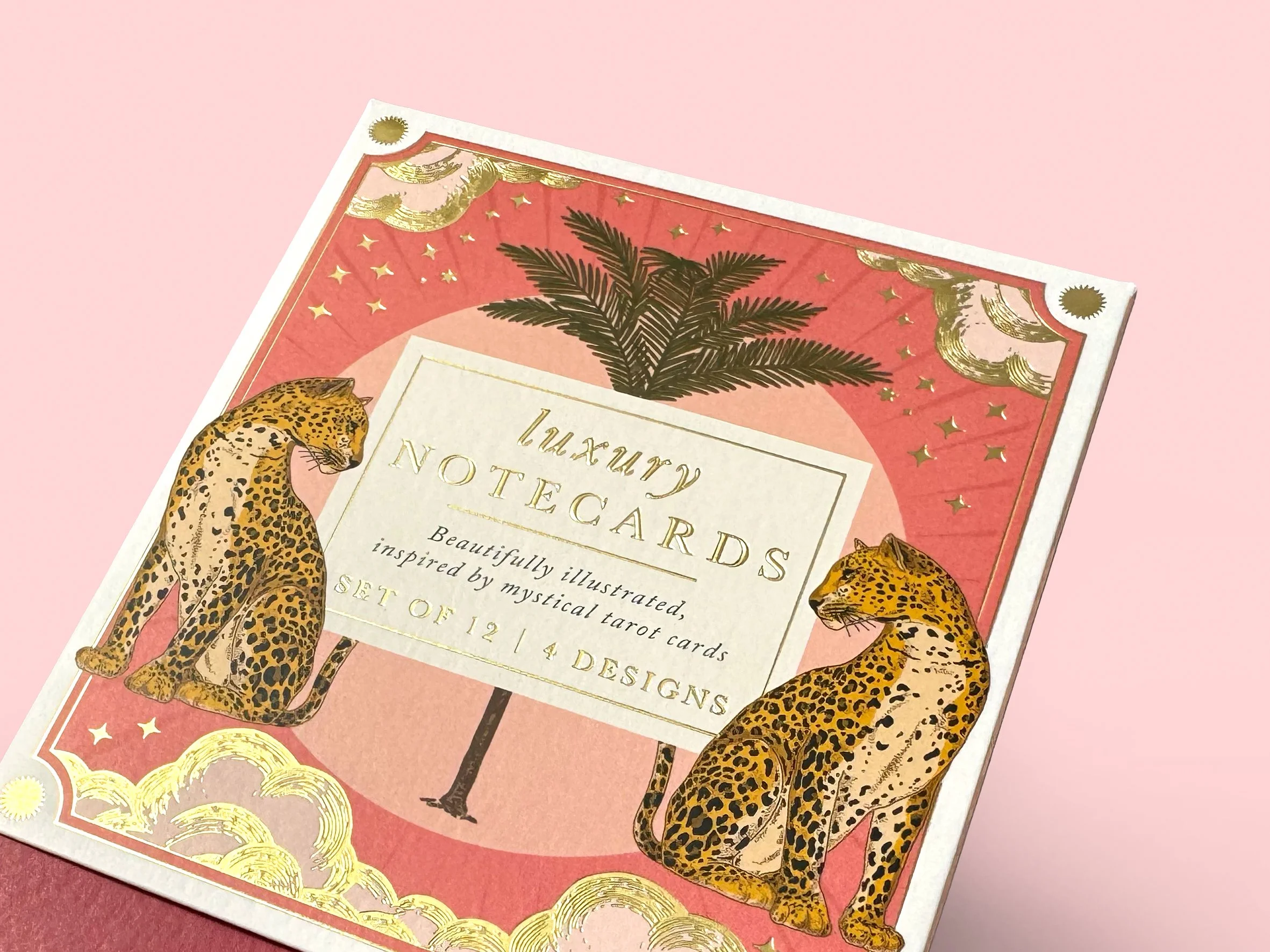 Close-up of a colorful tarot card set featuring illustrations of two leopards, a palm tree, and stars on a pink background. Carton packaging produced by Windles Packaging.
