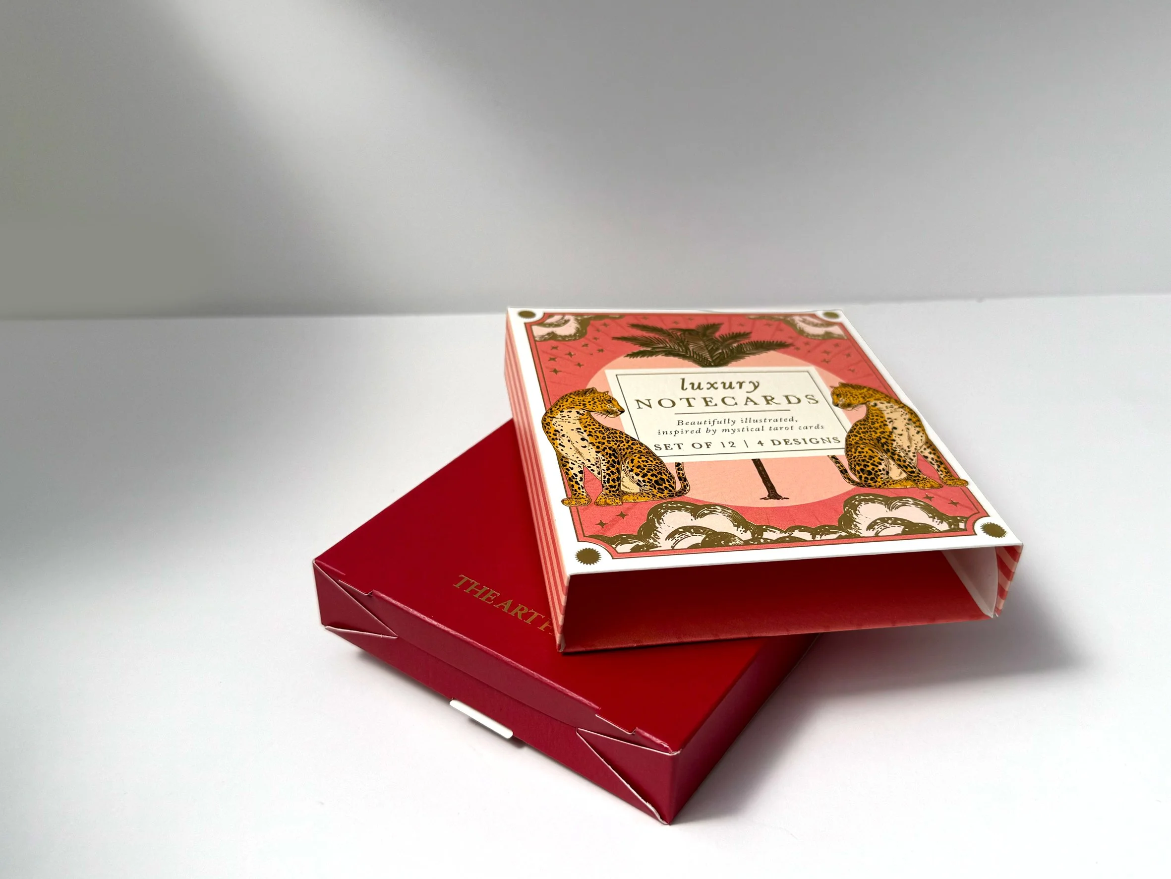 A deck of luxury illustratednotecards with pink and gold packaging, featuring leopard illustrations, placed on top of a red box on a white surface. Carton packaging produced by Windles Packaging.