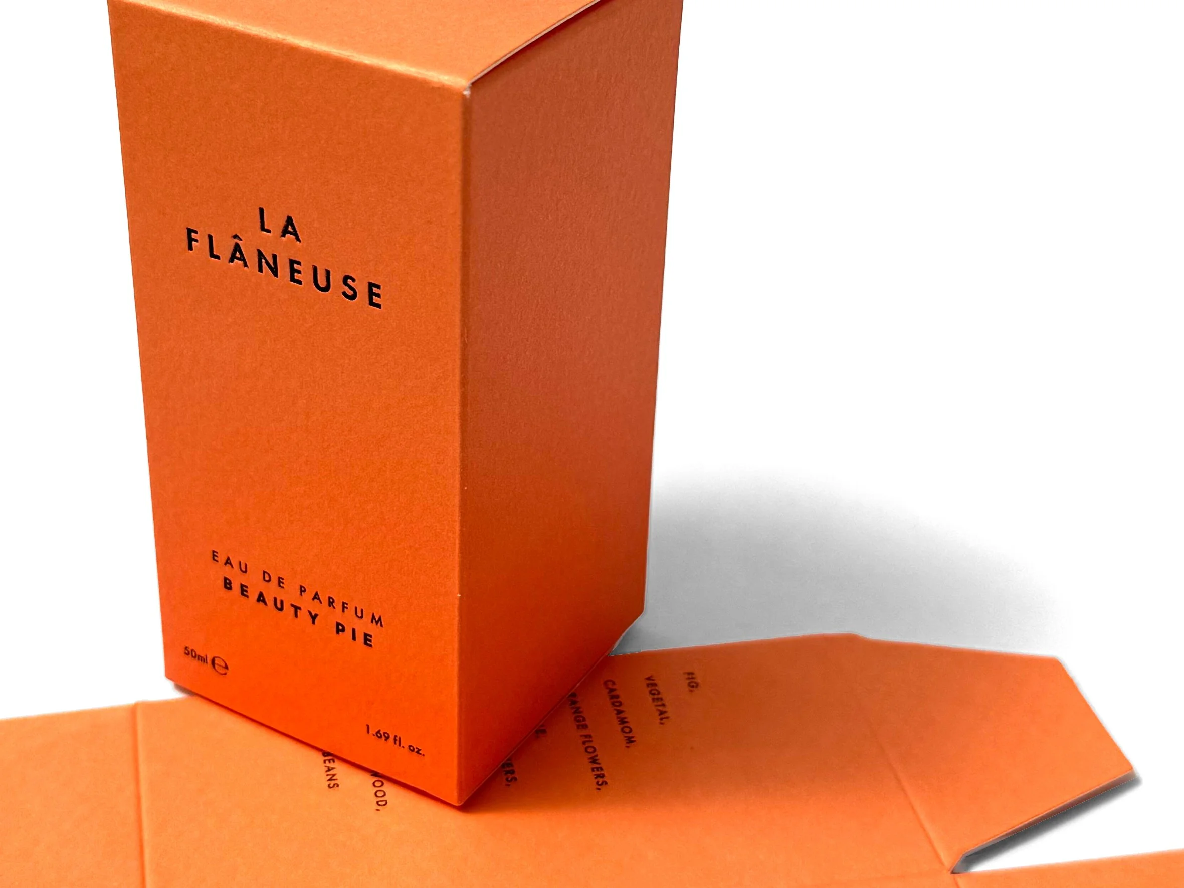 Close-up of orange packaging for La Flâneuse perfume, showing text indicating it is a 50ml bottle of Eau de Parfum named Beauty Pie, with some text partially visible on the side.