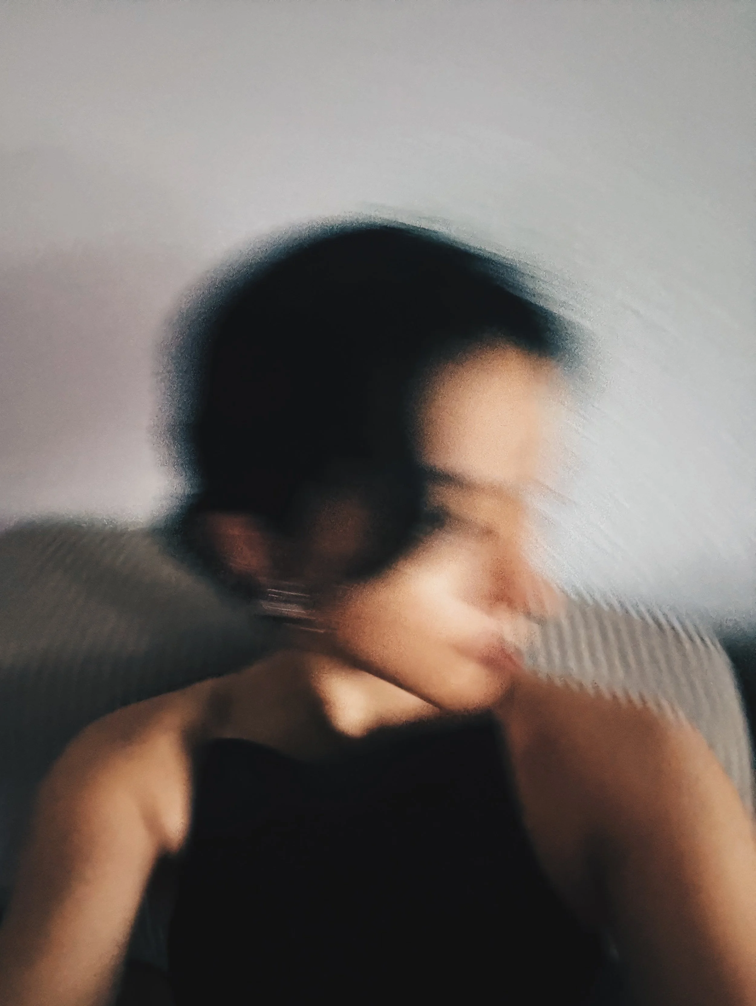 A blurry, abstract photograph of a person's face and hand against a plain background.