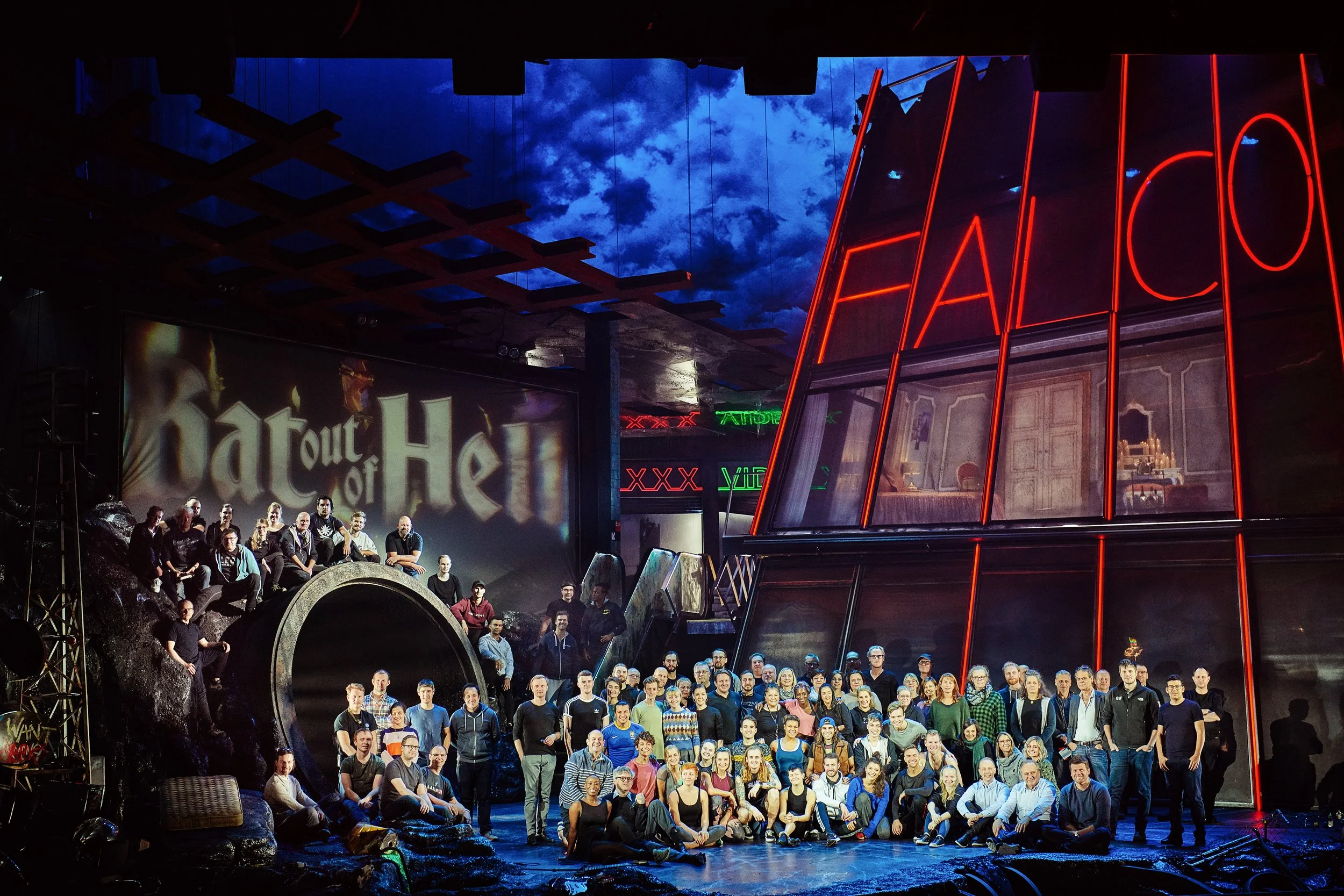 Gruppenfoto bei einer Bühne, unten stehen Menschen, oben Schauspieler auf der Bühne. Im Hintergrund eine Projektionswand mit dem Wort 'Bat Out Of Hell.