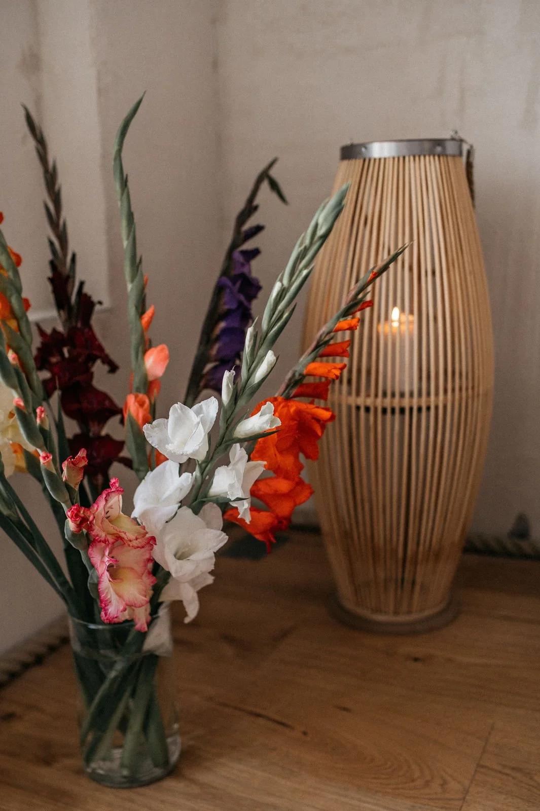 Blumenstrauß mit Gladiolen in einer Vase und eine große Laterne mit Kerze im Hintergrund.