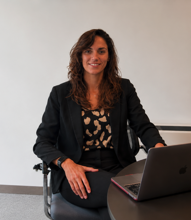 Mujer sentada en una oficina, sonriendo, con una laptop en una mesa redonda.